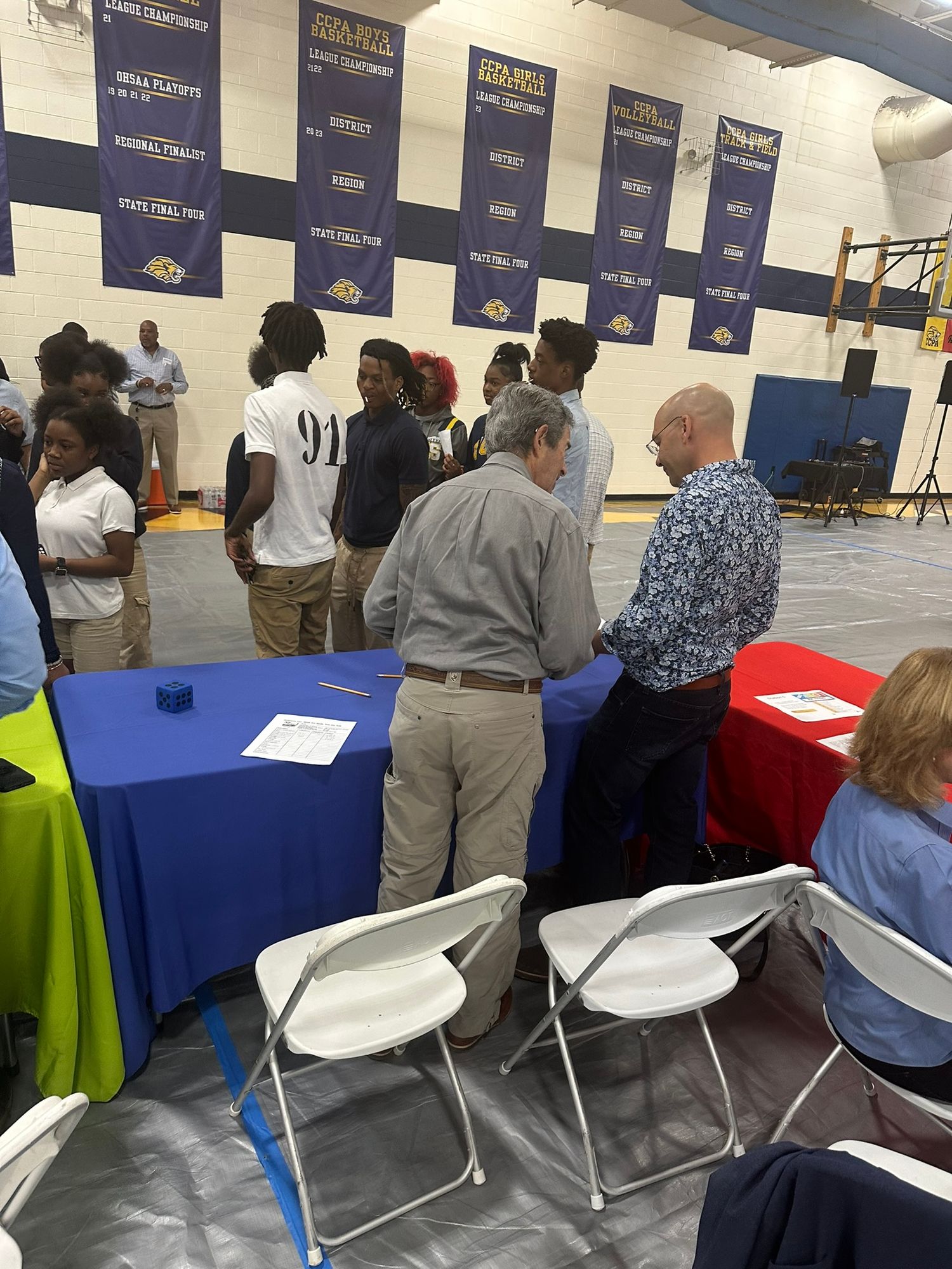 Students and adults network at a school career fair in a gymnasium with blue and gold banners.
