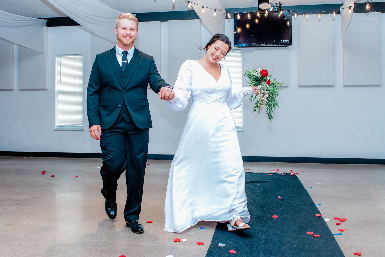 Bride and groom walking hand in hand down the aisle with rose petals on the floor at their wedding reception.