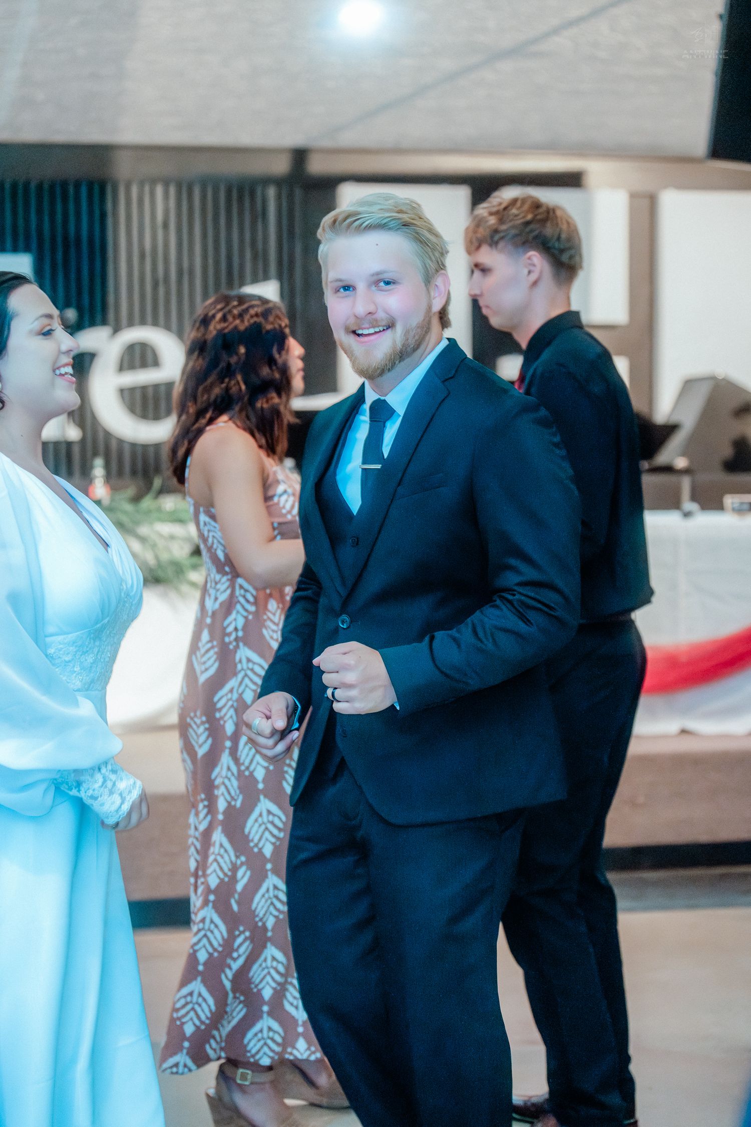 Smiling blond man in navy suit socializing at elegant wedding reception venue.