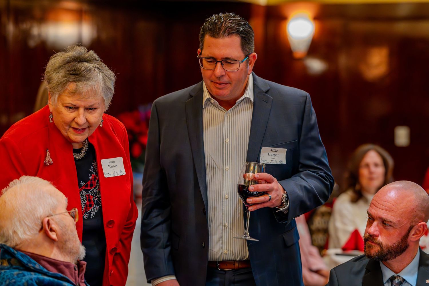 Professionals networking at a formal dinner event, with a woman in red and a man in a blue suit holding a wine glass.
