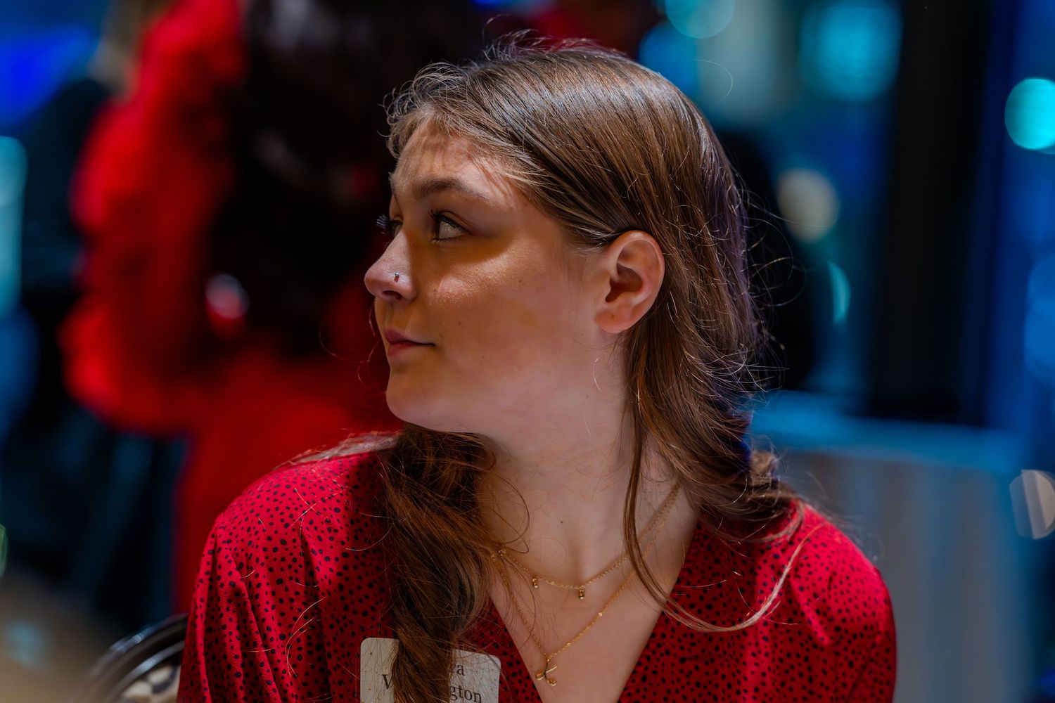 Young woman in red sequin top with braided hair, looking sideways in a dimly lit venue.