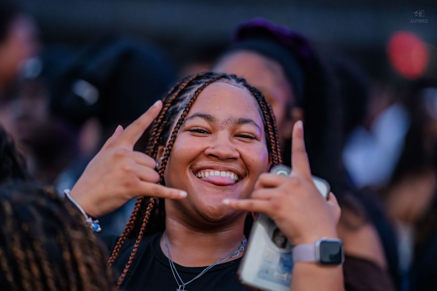 Smiling young woman with braided hair making hand gestures at an outdoor event.