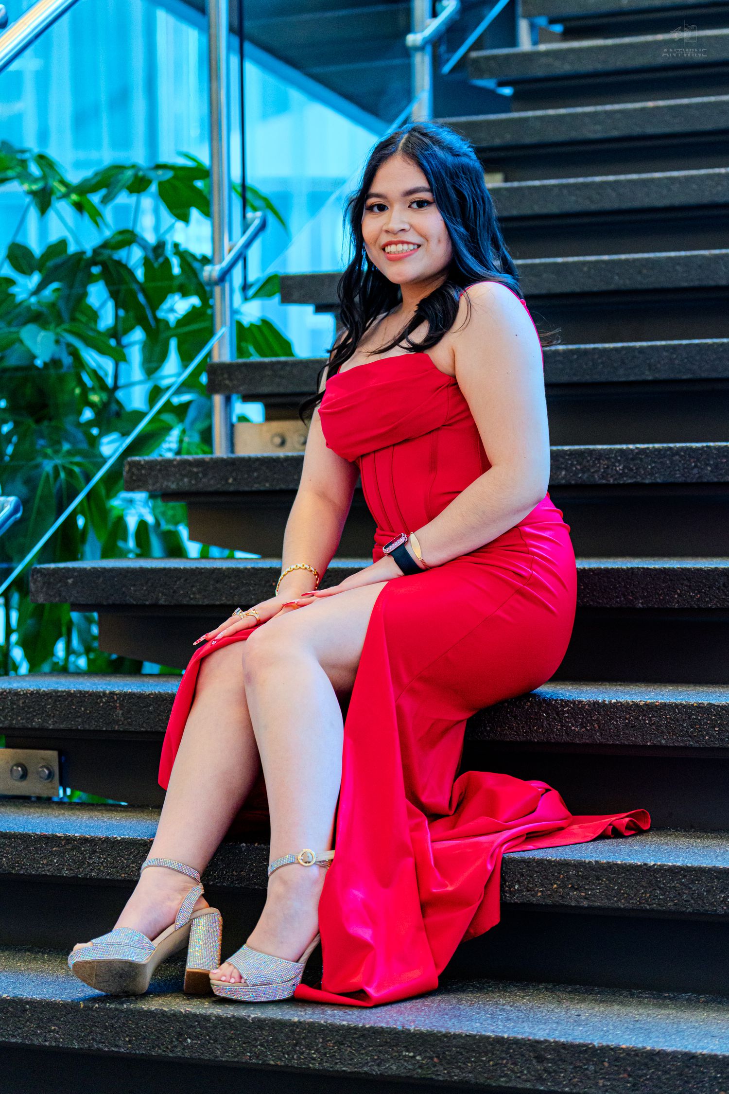 Woman in red strapless formal dress sitting on stairs wearing gold heels.