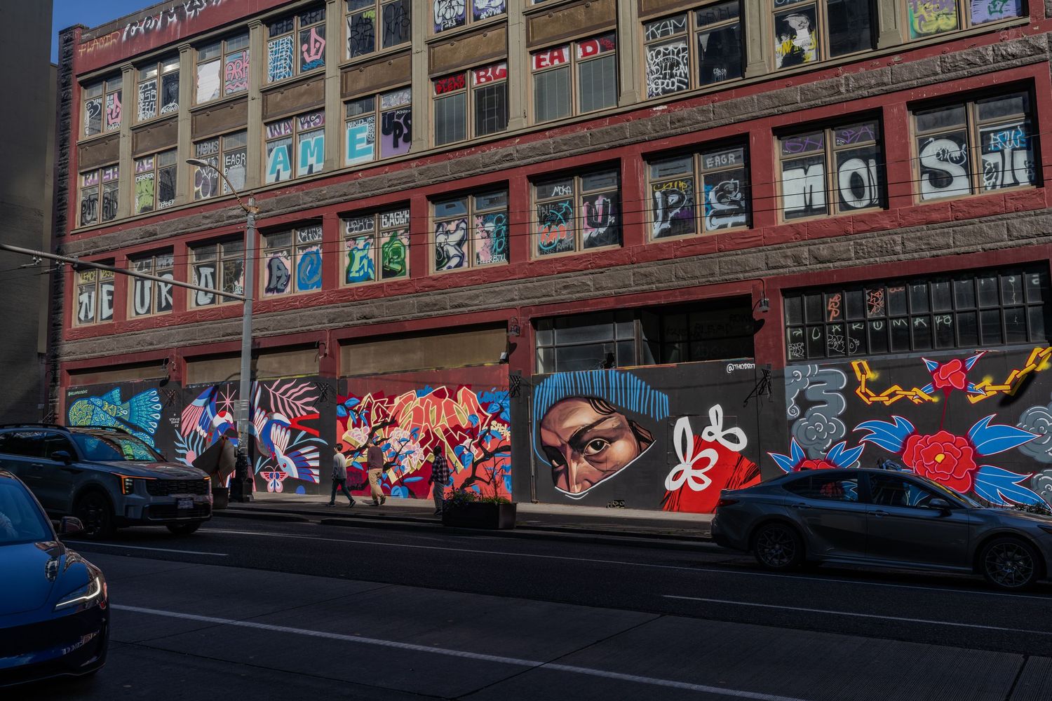 Colorful street art murals cover the exterior walls of a building along a busy urban street.