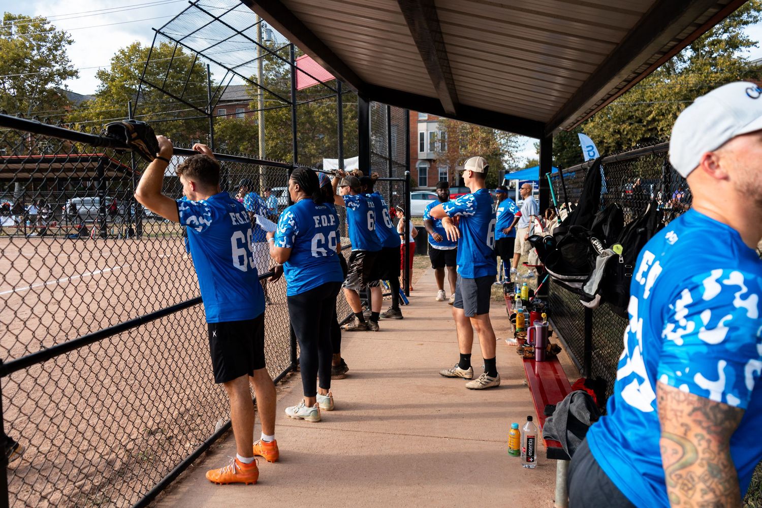 Softball team members in matching blue FOP jerseys cheer from the dugout during a charity game.