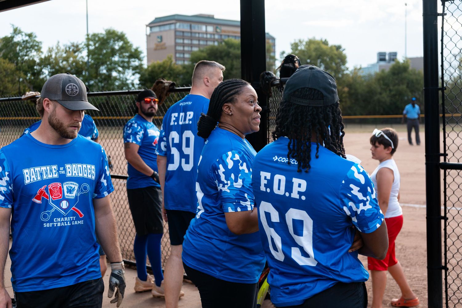 A team wearing blue F.O.P. number 69 jerseys gathers near a chain-link fence at a softball game.