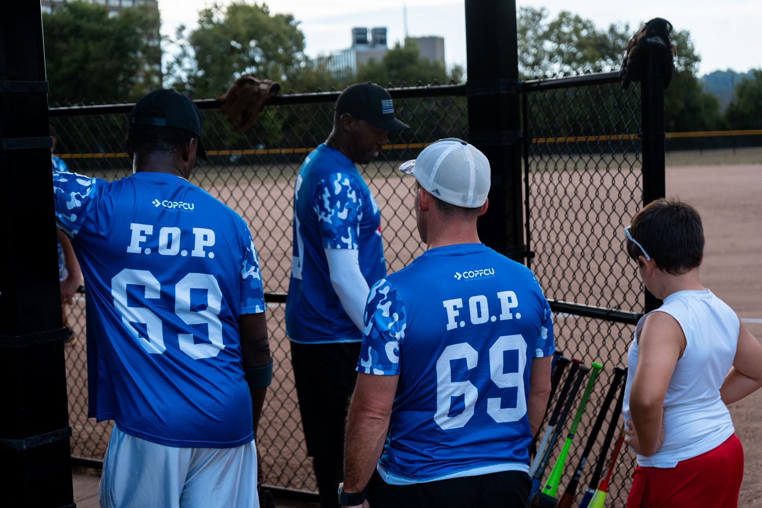 Players wearing F.O.P. 69 blue jerseys at a softball game near a chain-link fence.
