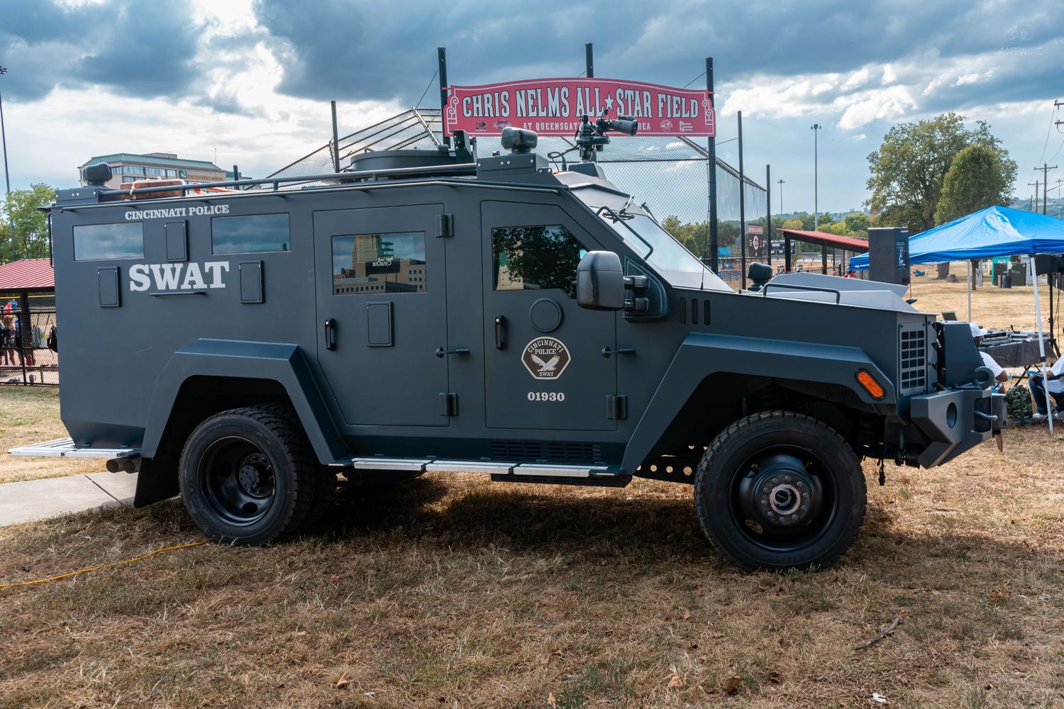 A gray SWAT armored tactical vehicle displayed outdoors at a public event with a red banner in the background.