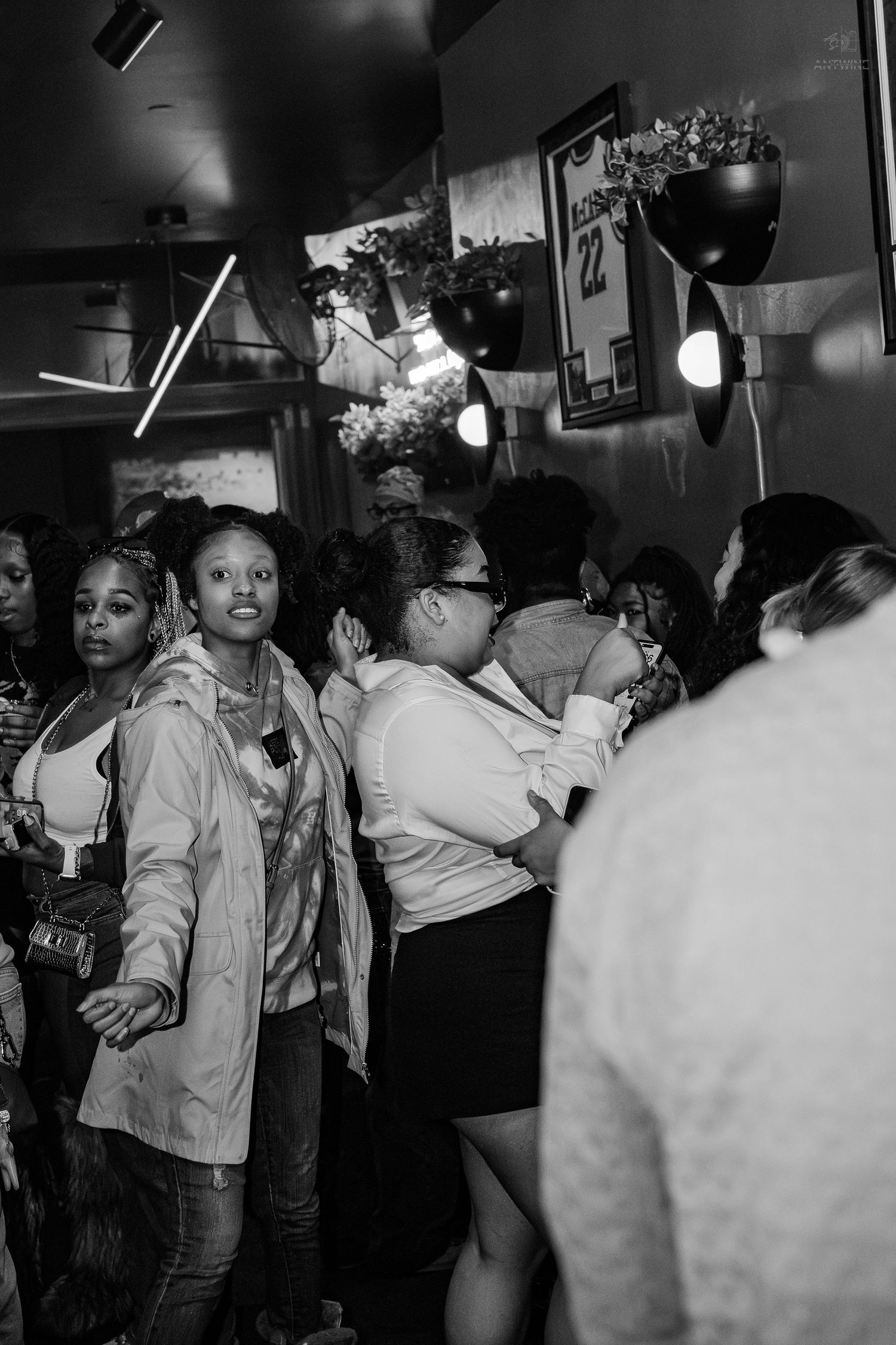 Black and white photo of a group of young women socializing indoors at a casual gathering or event.