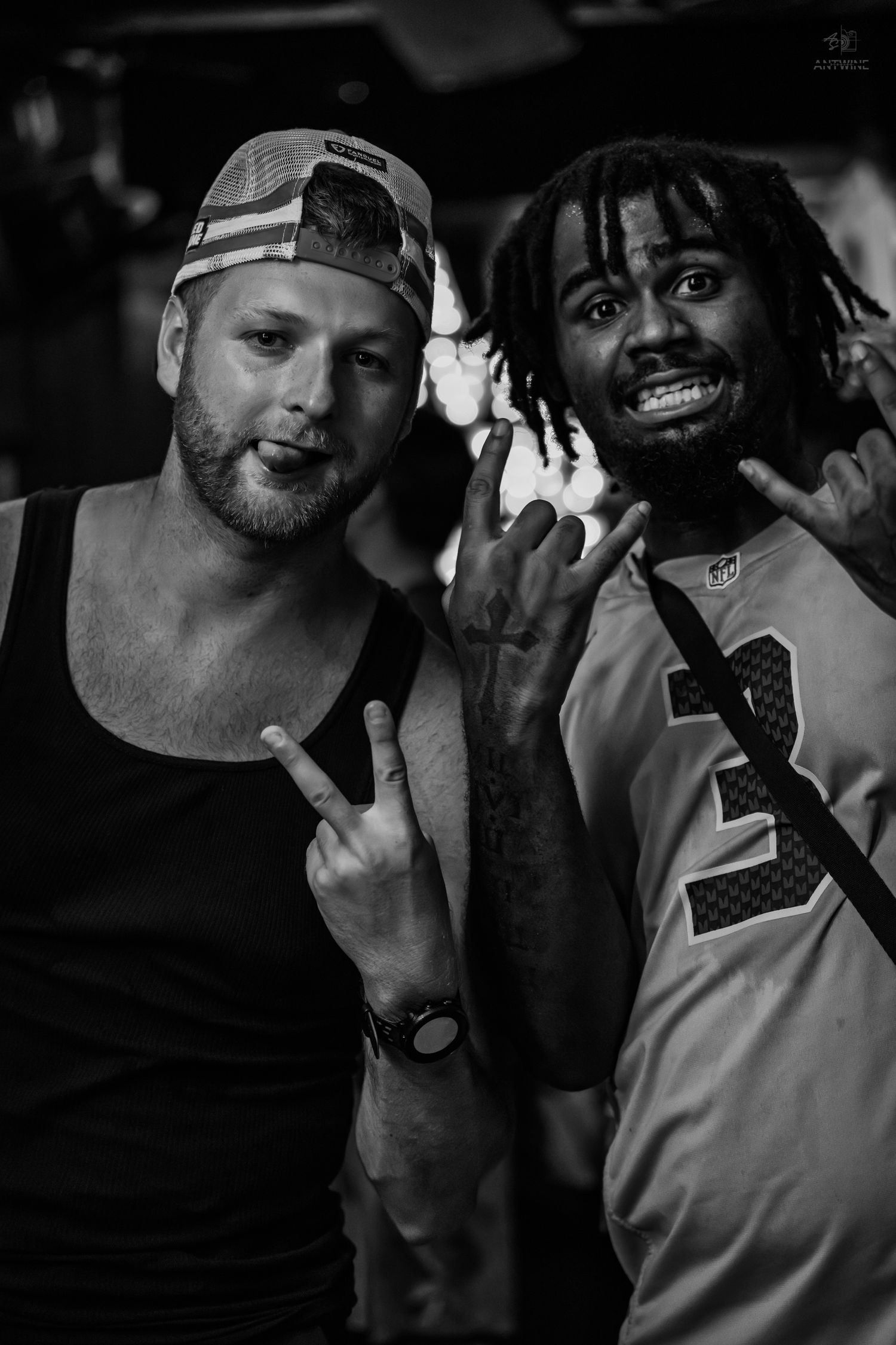Two men posing together making hand gestures in a black and white nightclub photo.