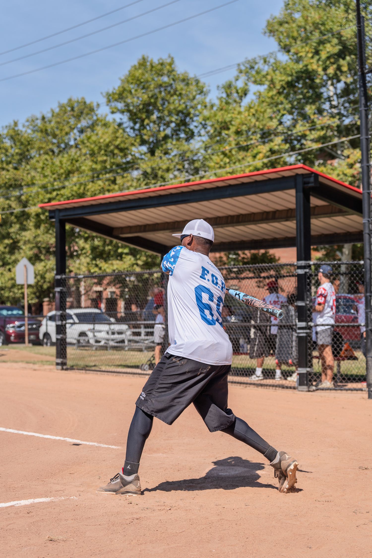 Softball player in white number 60 jersey completing swing on sunny dirt field.