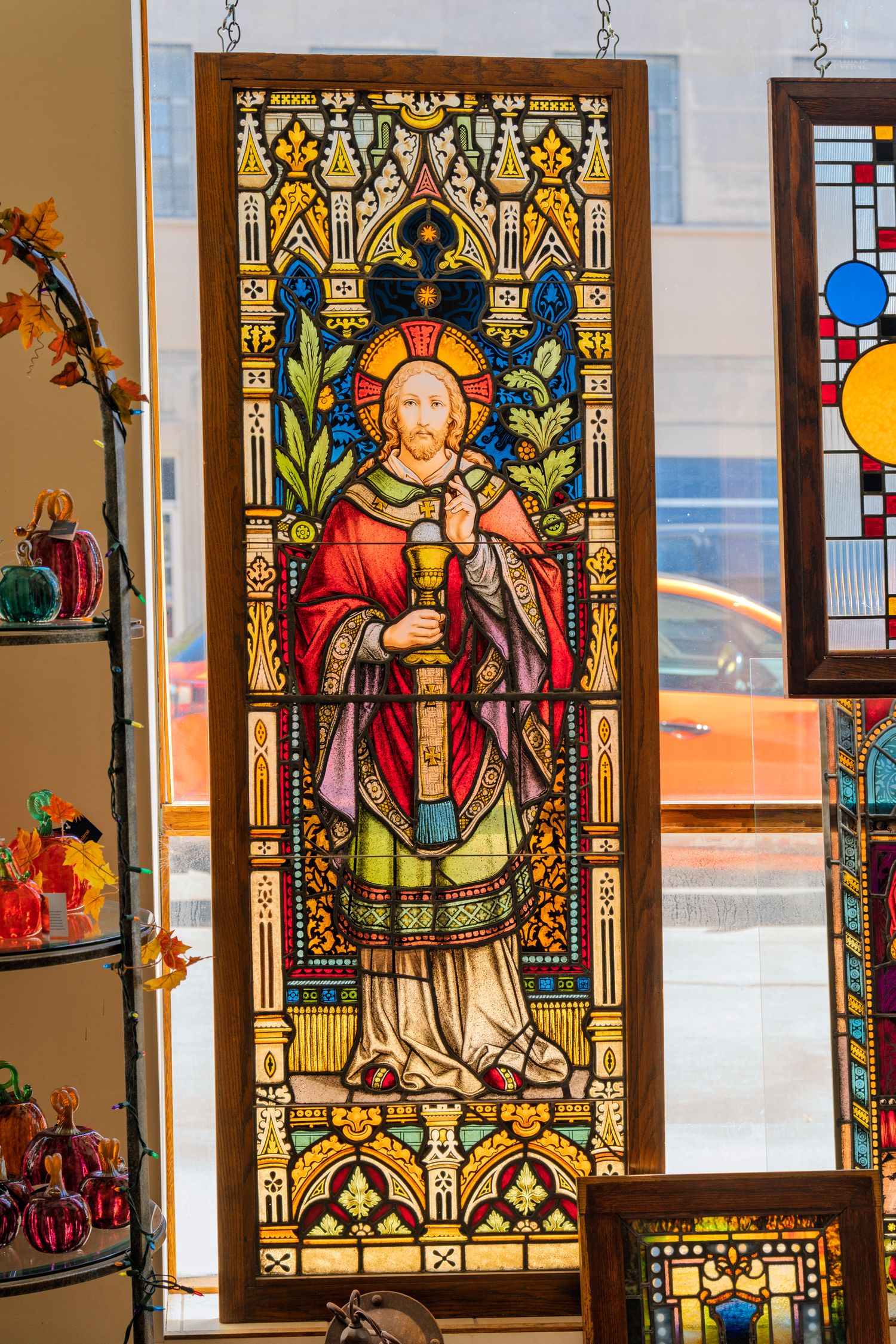 Colorful stained glass window depicting Jesus Christ in robes, displayed in an antique shop with decorative glass items.
