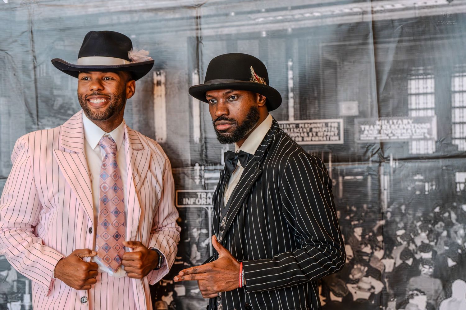Two men in vintage pinstripe zoot suits and fedora hats pose confidently in a retro-styled color photo.