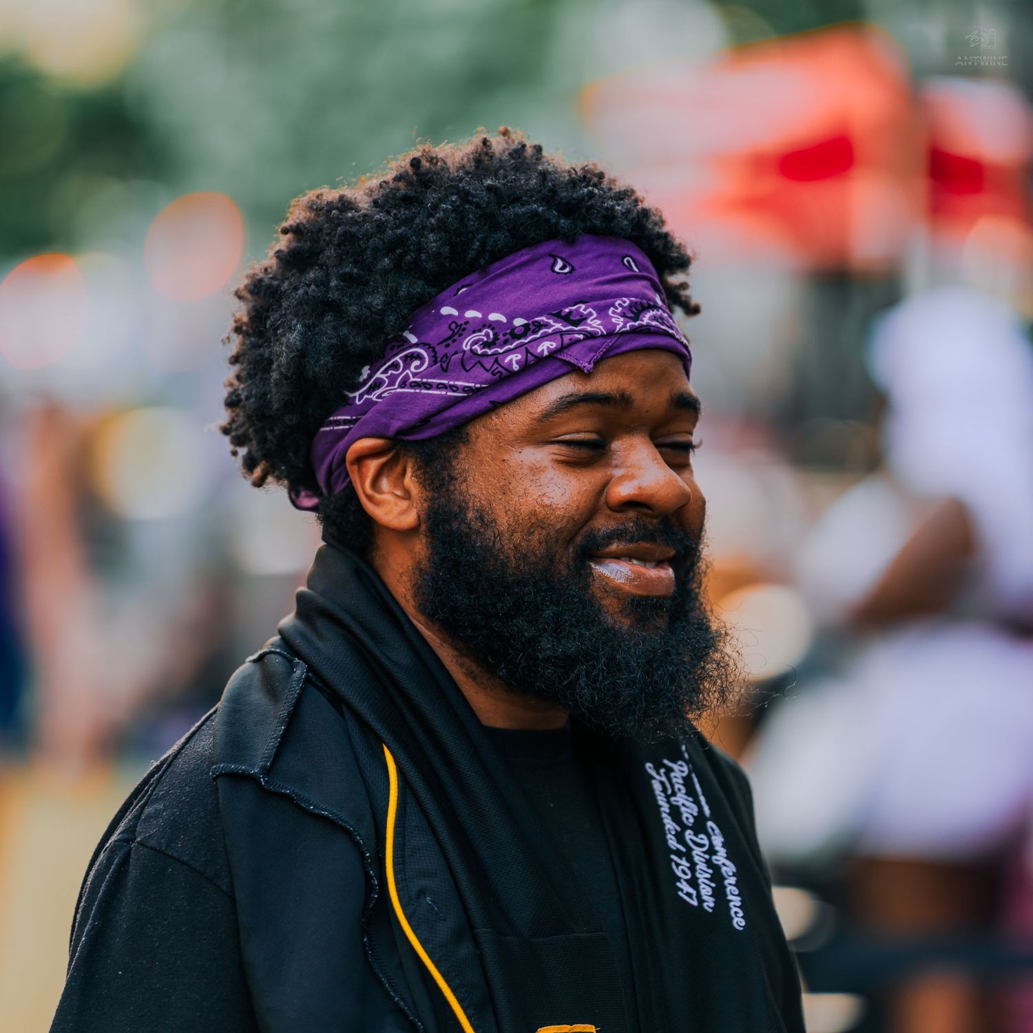 Smiling Black man with a full beard wearing a purple bandana headband at an outdoor festival.