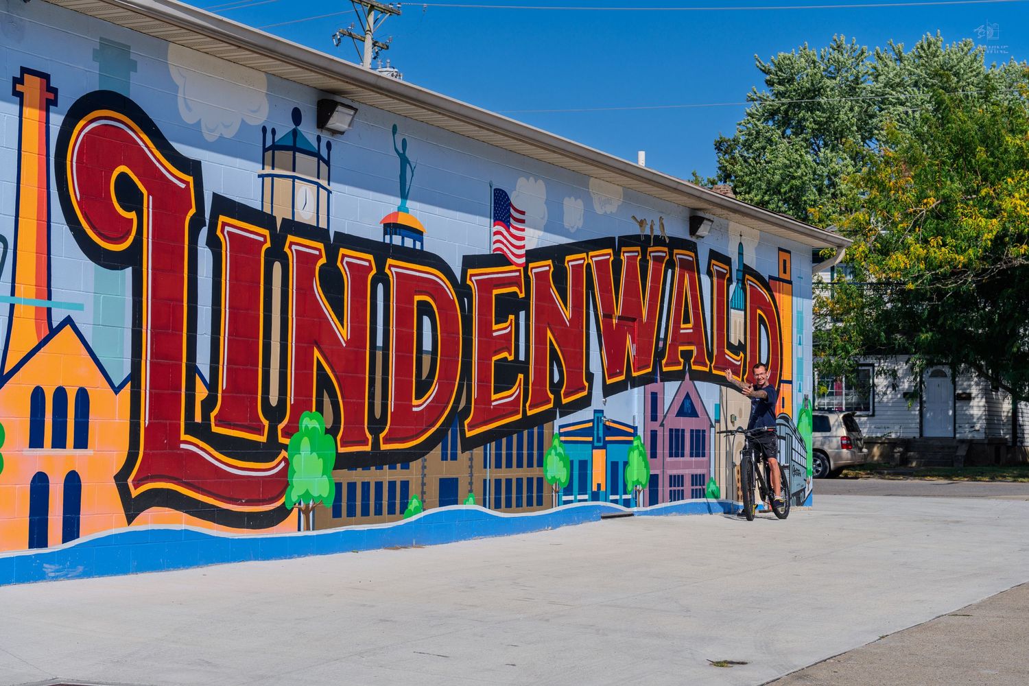 Colorful Lindenwald neighborhood mural on a building wall with vibrant lettering and cityscape artwork on a sunny day.