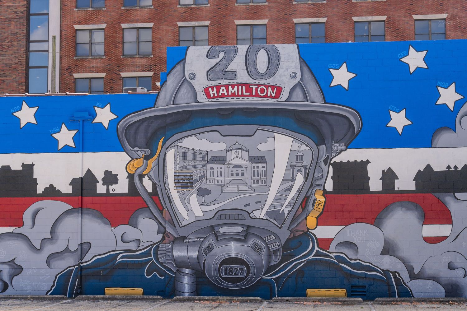 Mural of firefighter in helmet labeled Hamilton 20, with American flag design on urban wall.