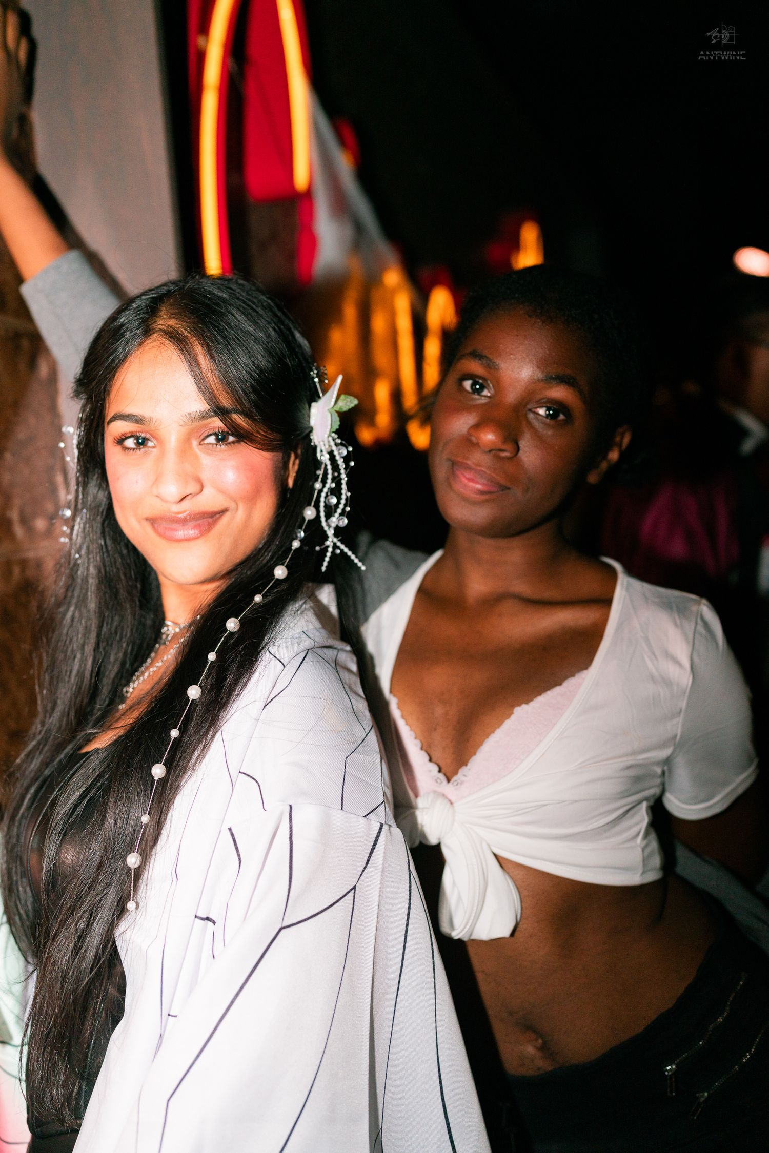Two women smiling back-to-back at a Halloween party, one in bridal attire with pearl hair accessories.