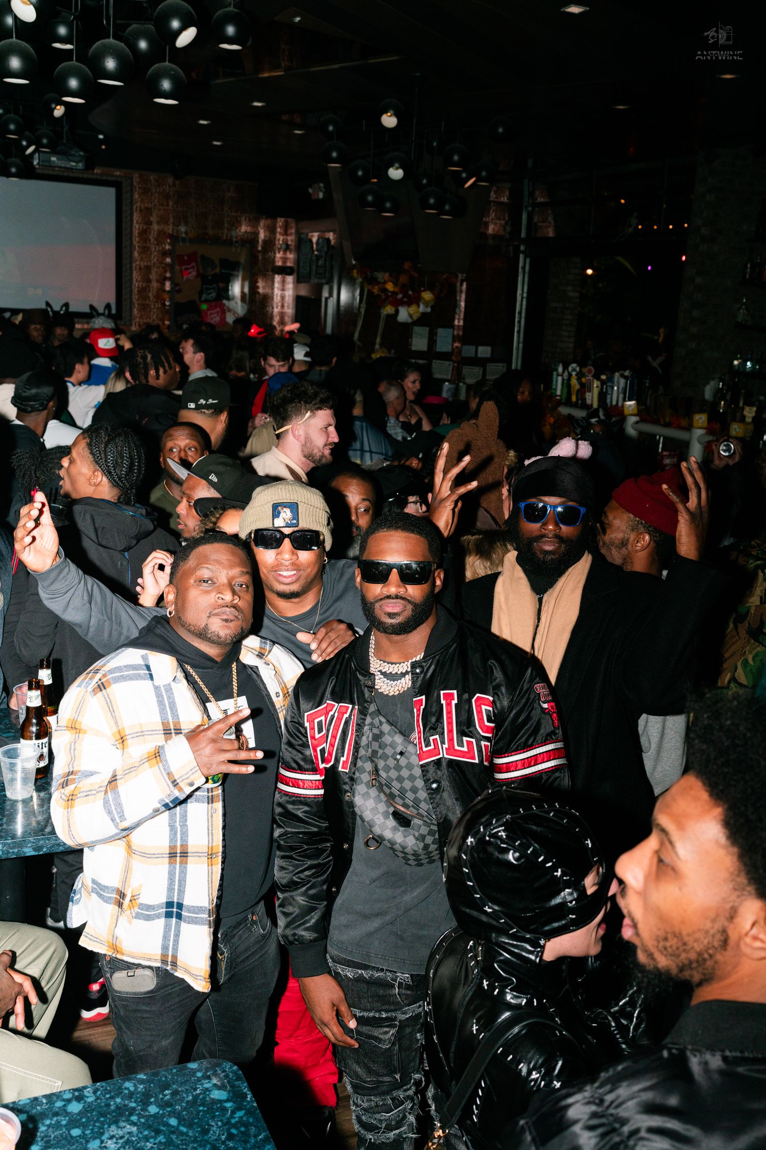 Men in streetwear posing together at a packed nightclub party.
