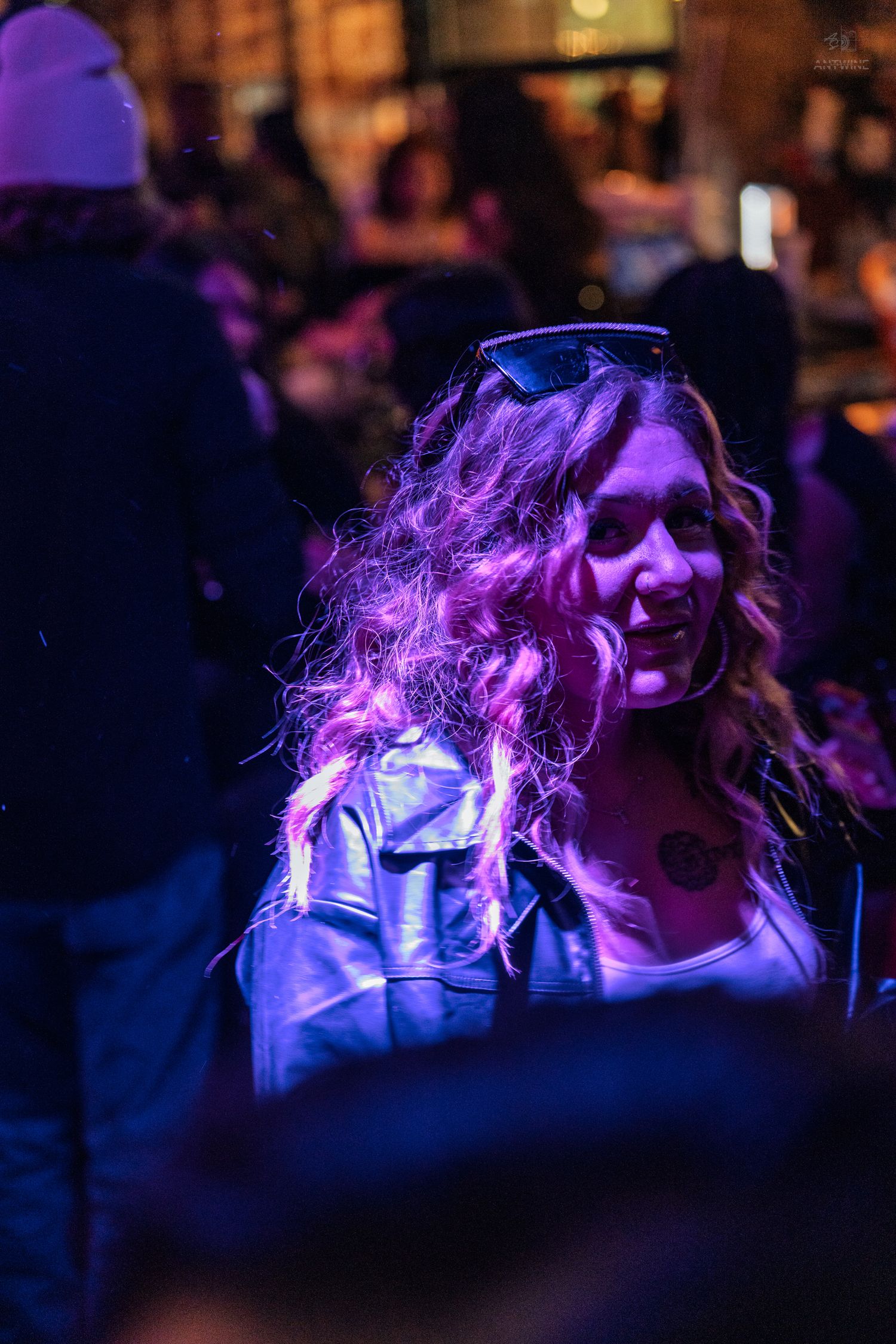 Woman with curly hair smiling under purple lights at a night event.