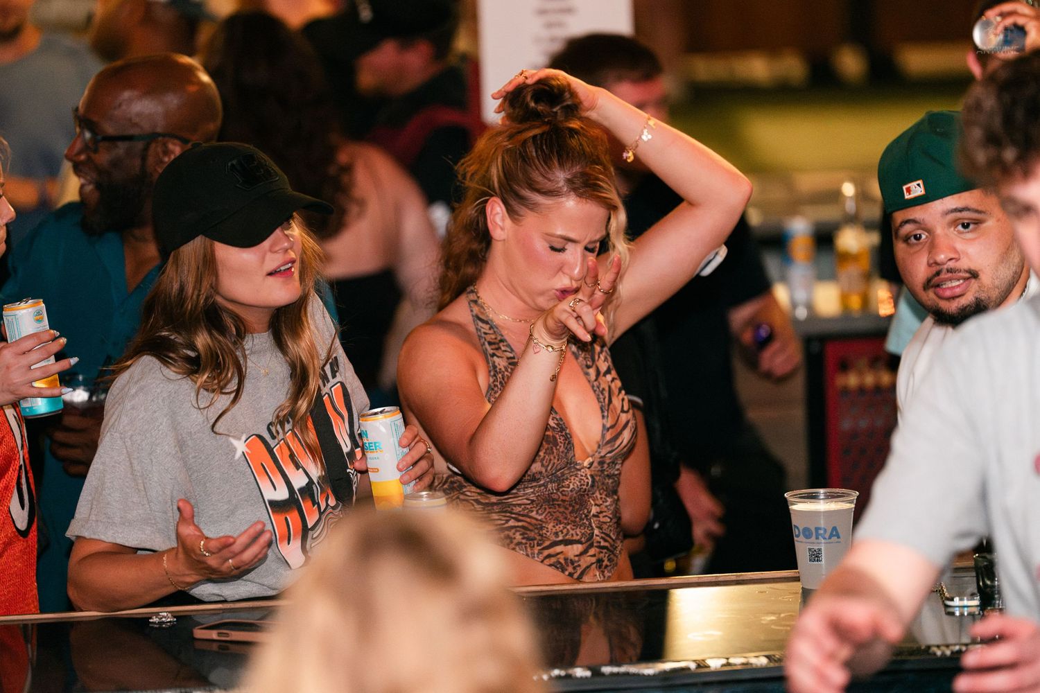 Women socializing at a bar, one in a sequined top fixing her hair at a crowded venue.