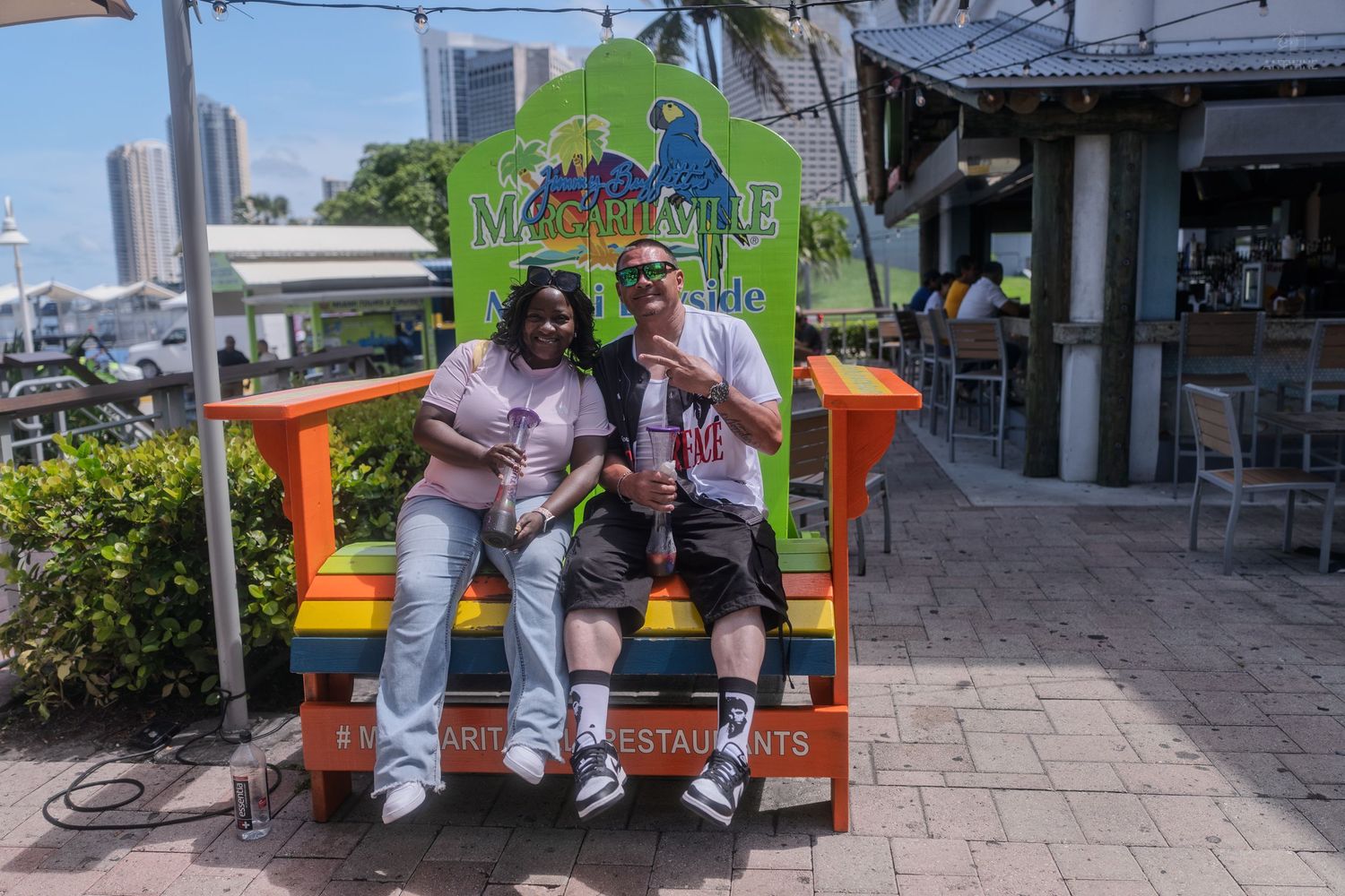 Couple poses together on a giant colorful Margaritaville restaurant chair outdoors on a sunny day.