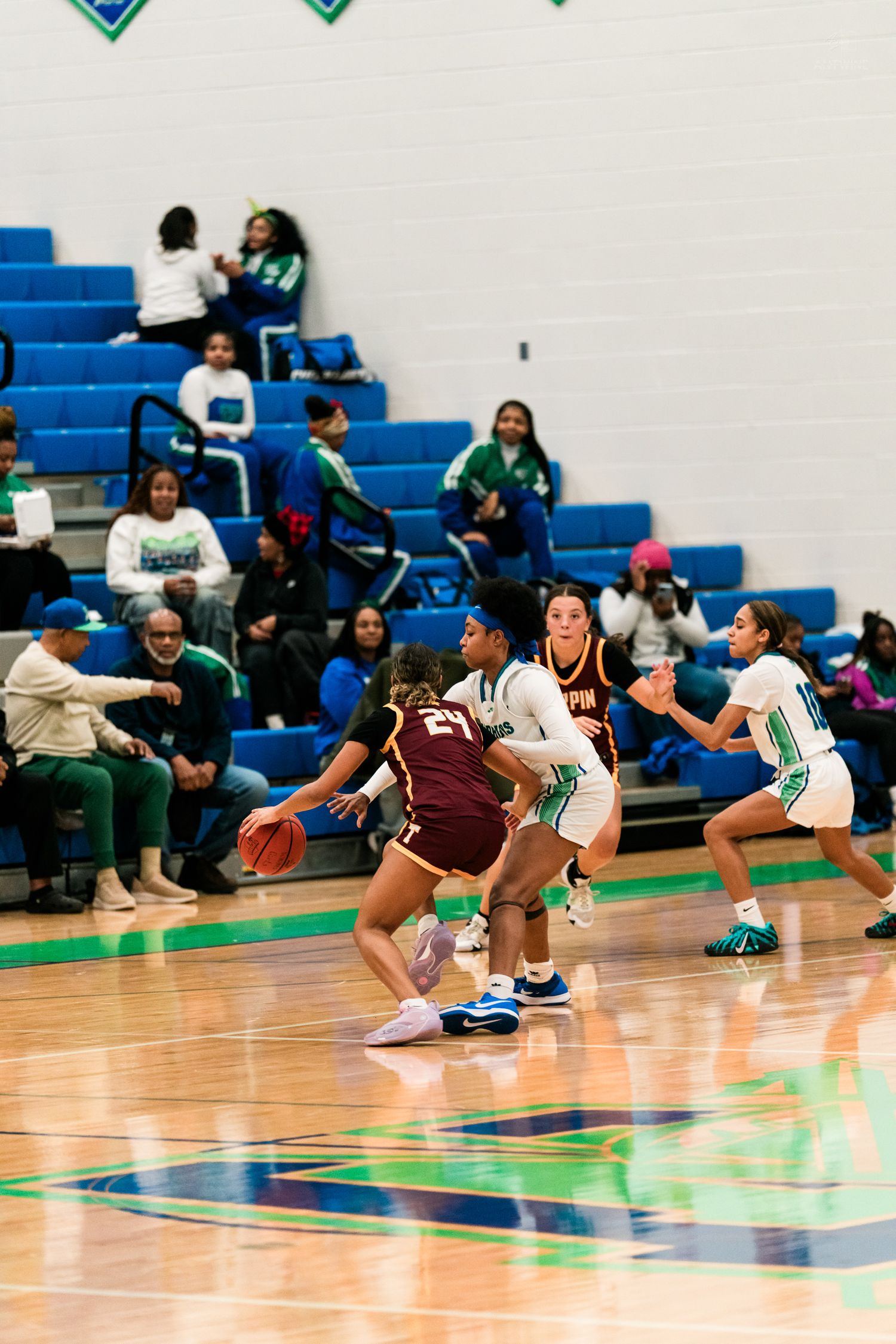 Female basketball players compete on the court as a maroon-uniformed player number 21 dribbles past defenders.