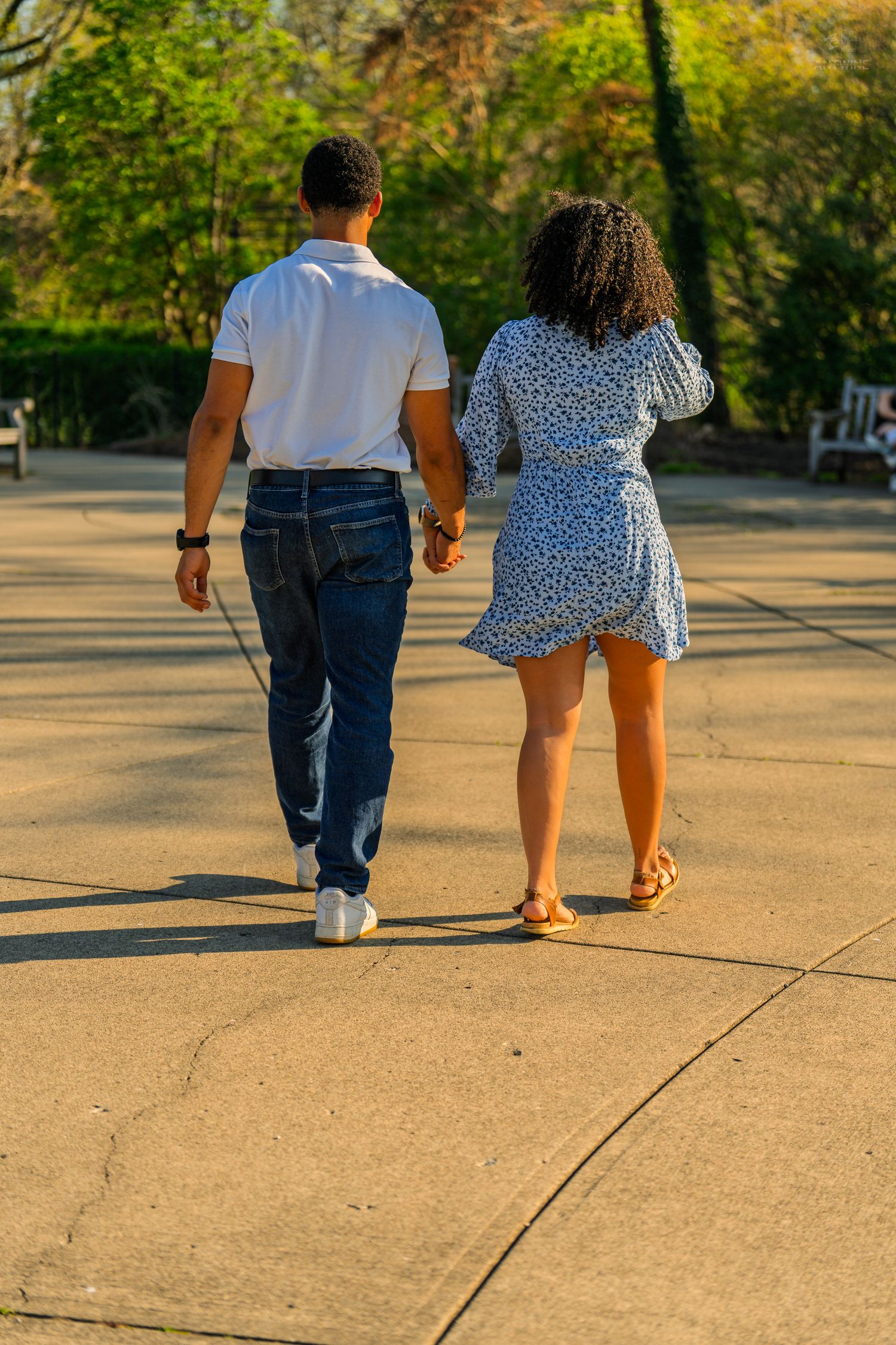 Rear view of a couple holding hands strolling along a golden sunlit park pathway together.