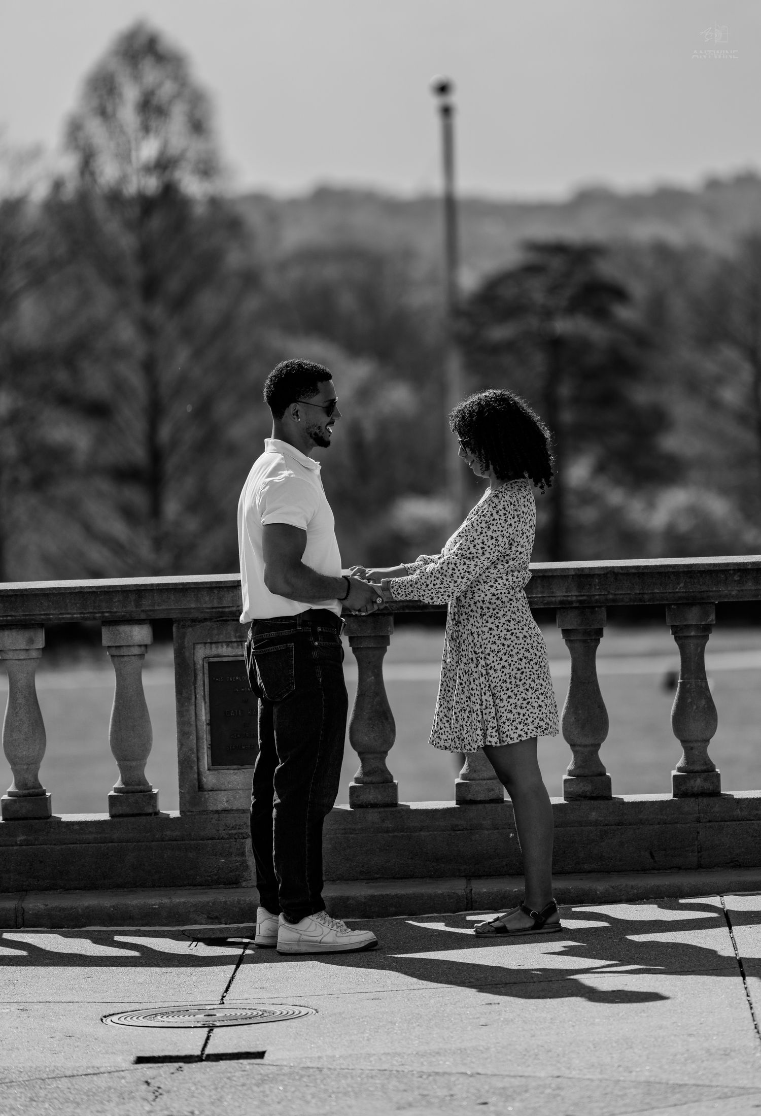 Black and white photo of couple holding hands on a stone balcony terrace in a park setting.
