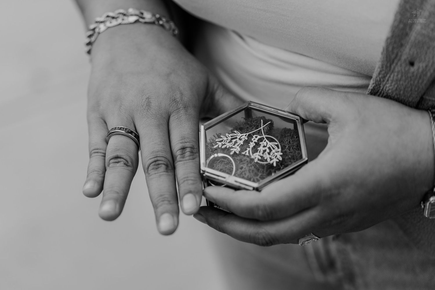 Black and white photo of hands holding a hexagonal glass jewelry box with rings inside.