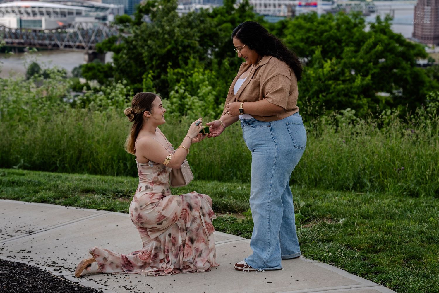 Woman in floral dress kneeling to propose to partner in color photo.