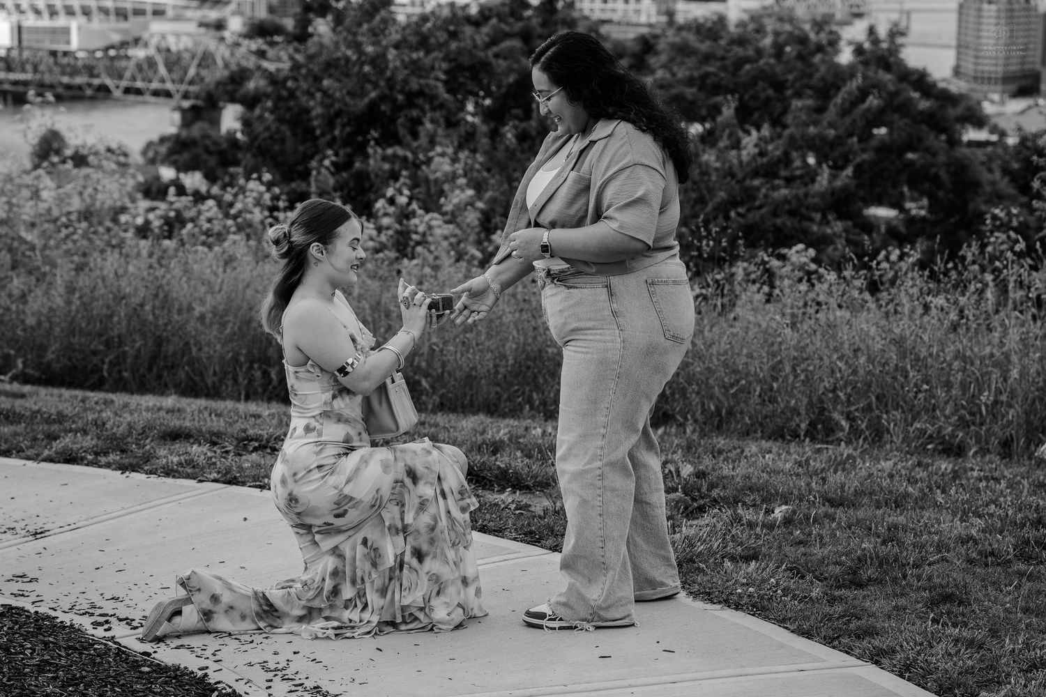 Black and white photo of woman proposing to partner near lush greenery.