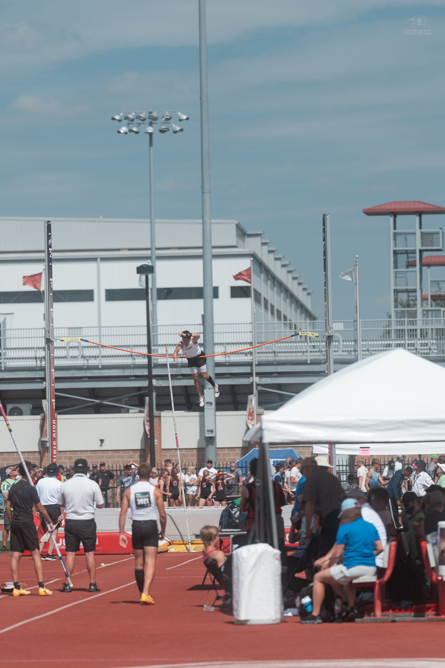 Athlete mid-vault during a pole vault competition at an outdoor track and field stadium.