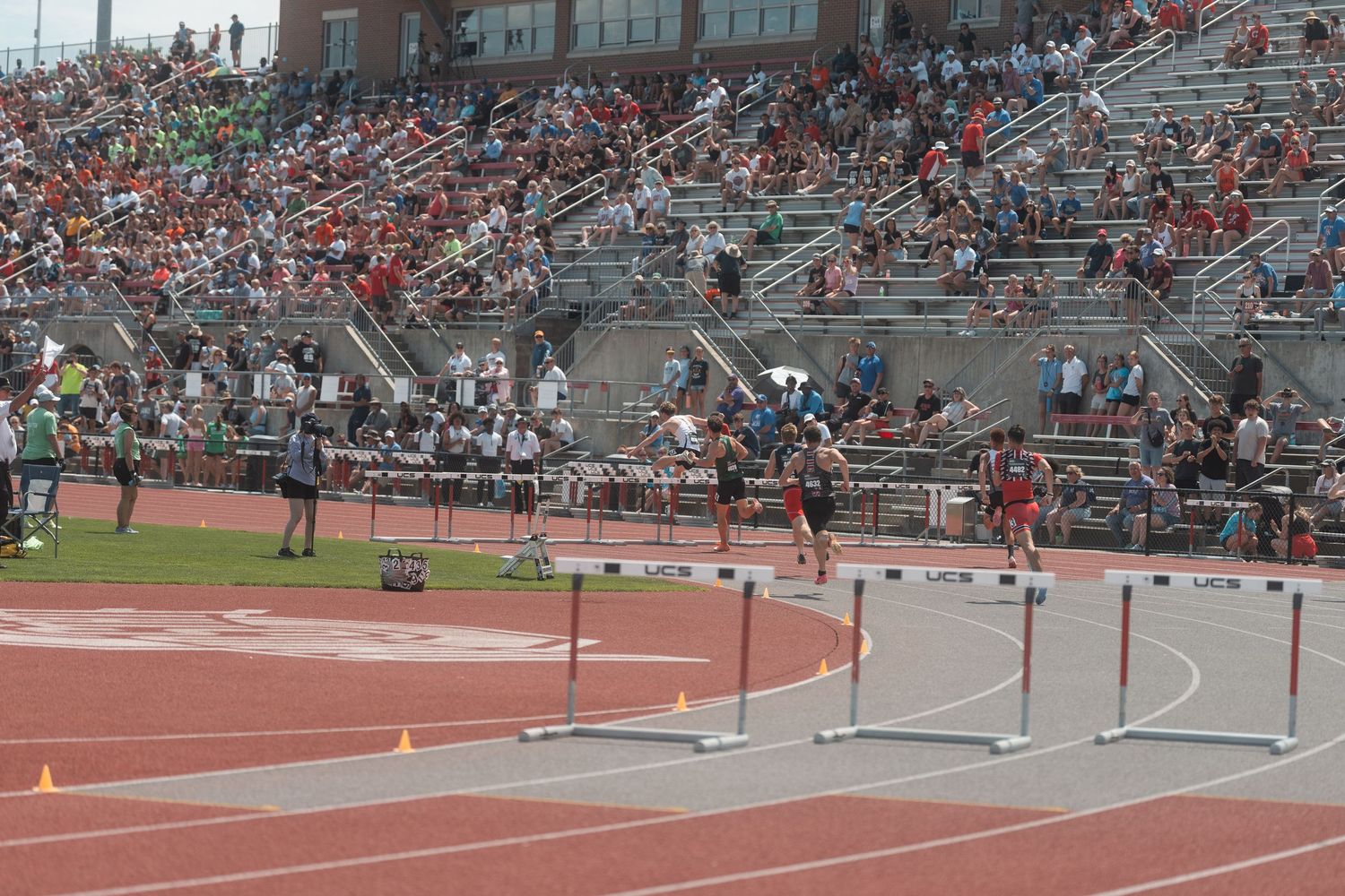 Competitors leap over hurdles at a packed Ohio State University outdoor track and field competition.