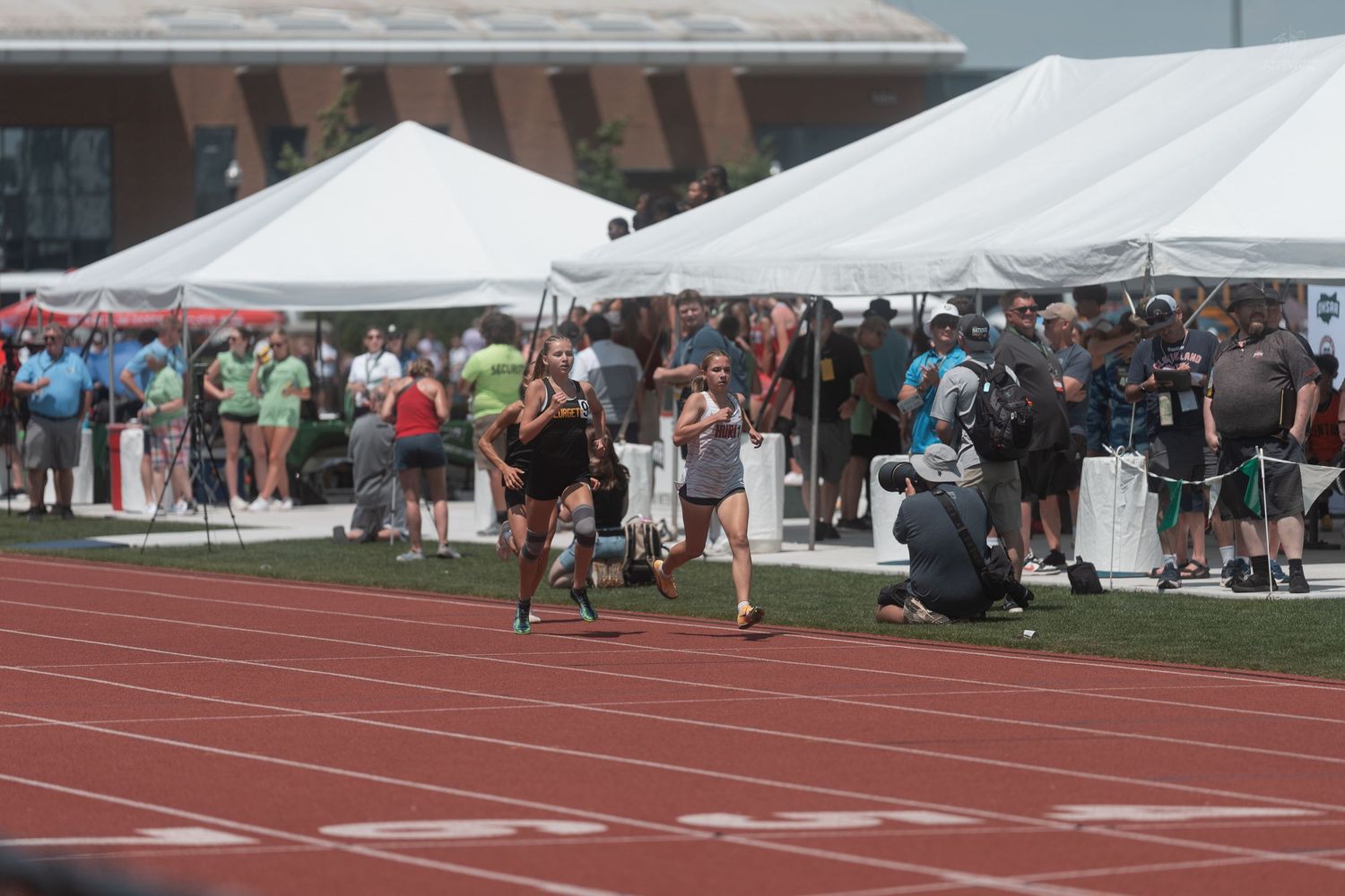 Two female athletes finish a track race near the finish line at an outdoor track and field championship event.