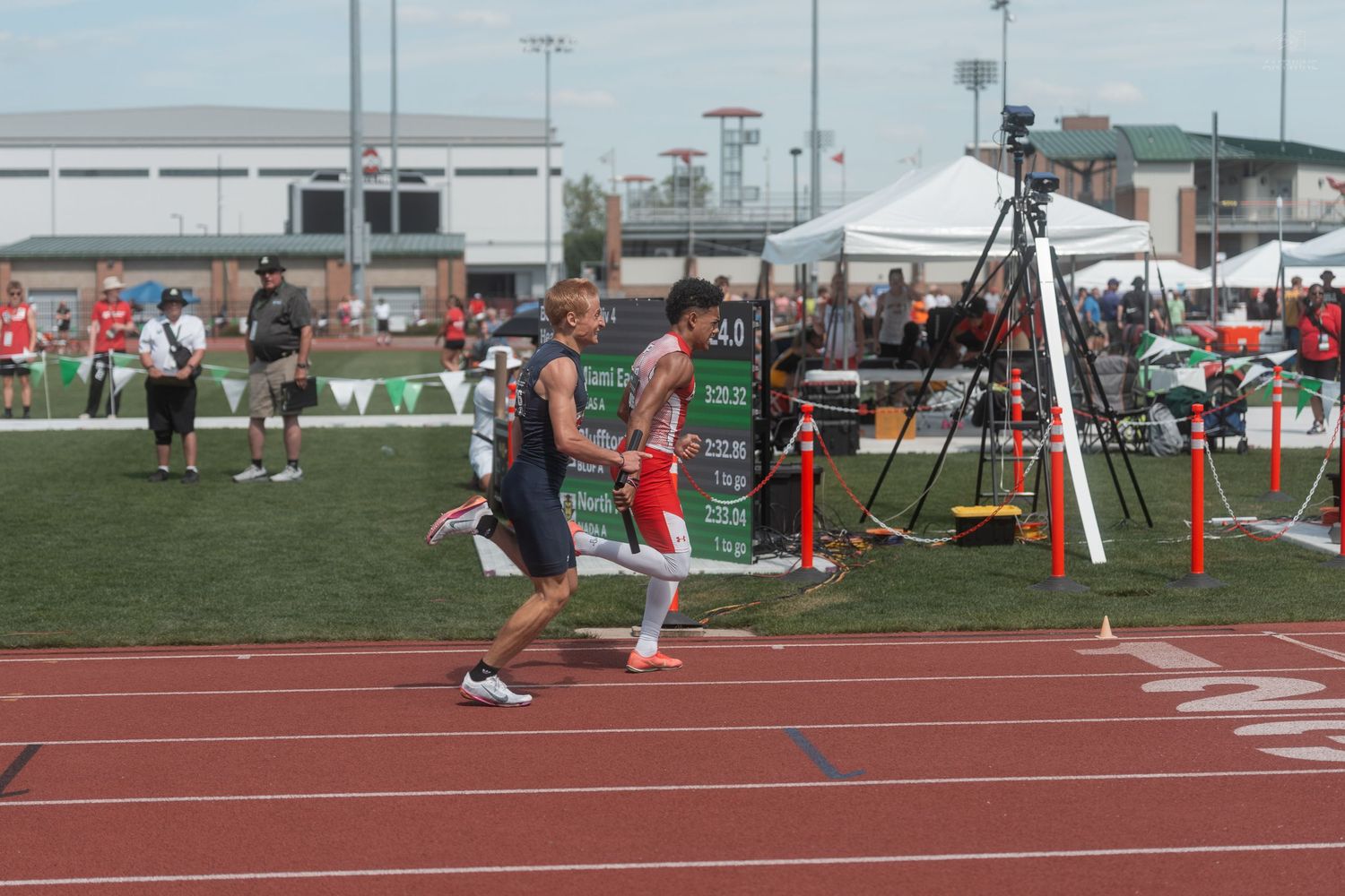 Two athletes running on a red track during a competitive track and field meet at an outdoor stadium.