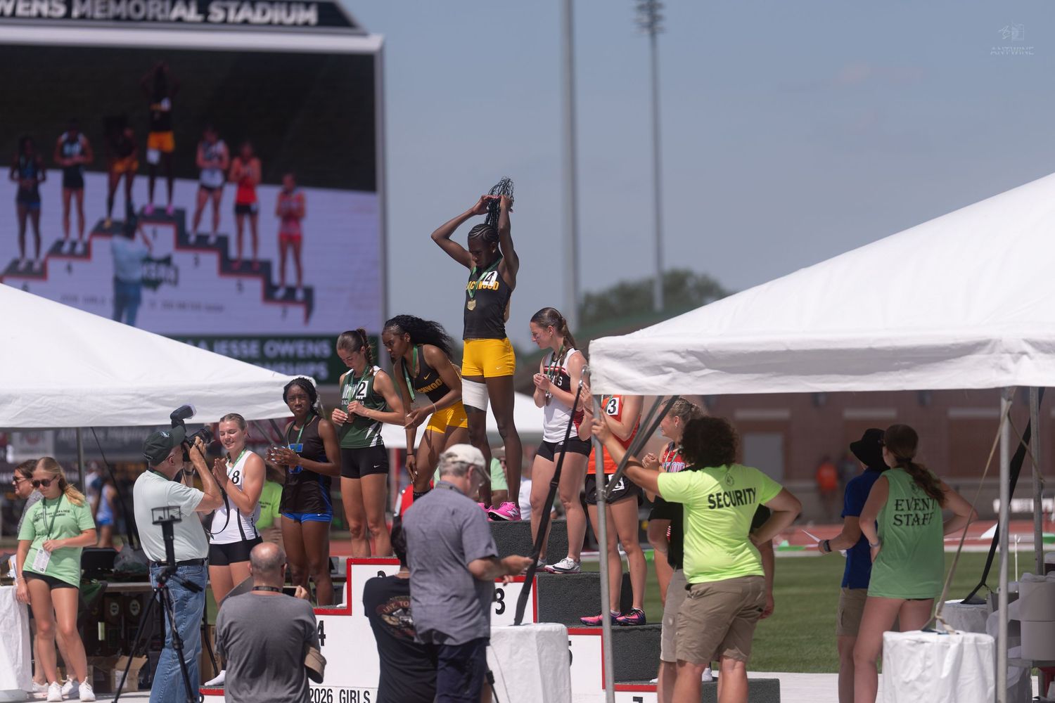 Athletes receive medals on a podium at an outdoor track and field championship awards ceremony.