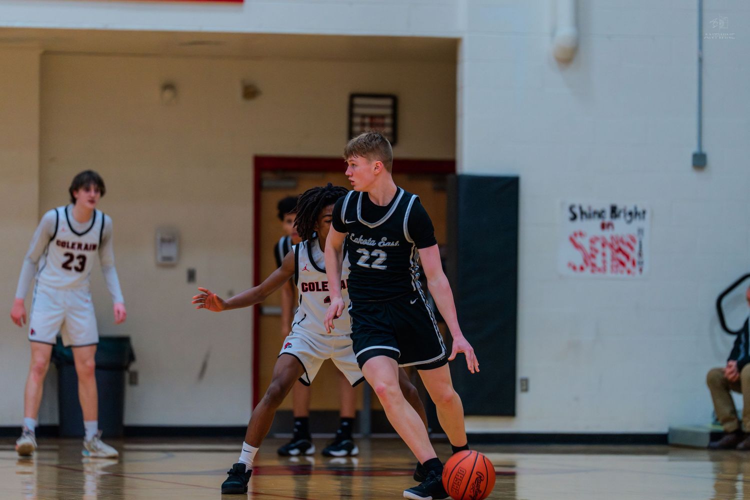 Lakers #22 dribbles ball during high school basketball game near Shine Bright sign.