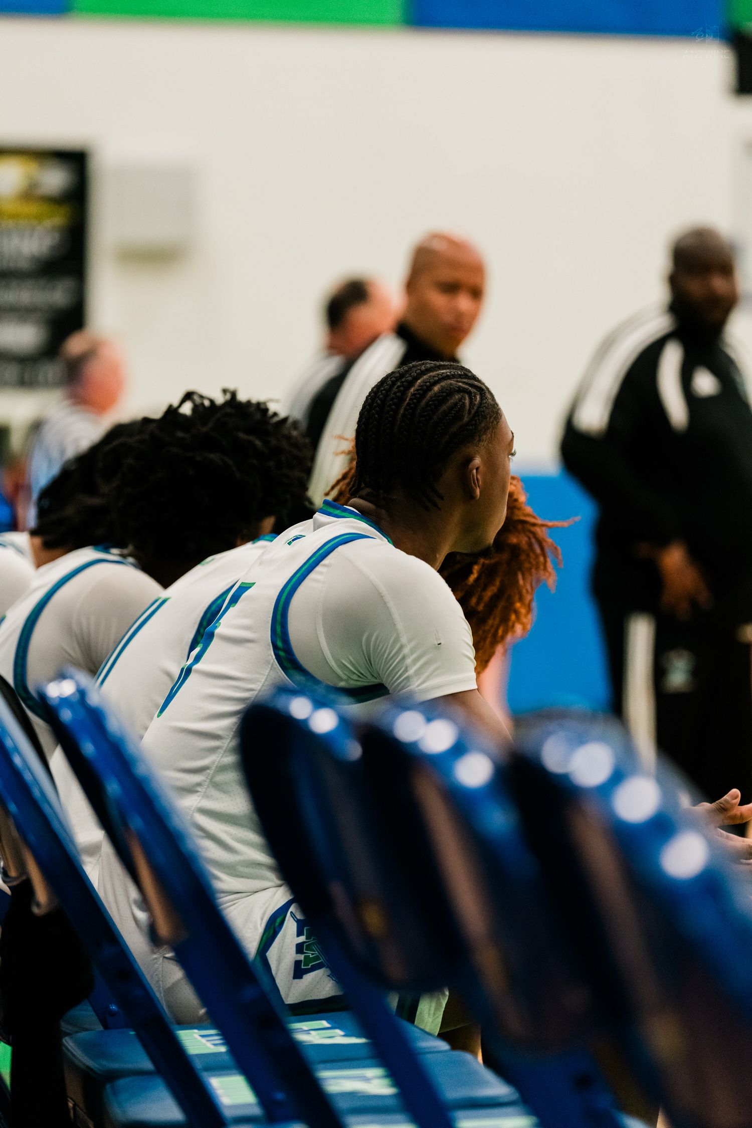 High school basketball players in white uniforms sitting on bench during game.
