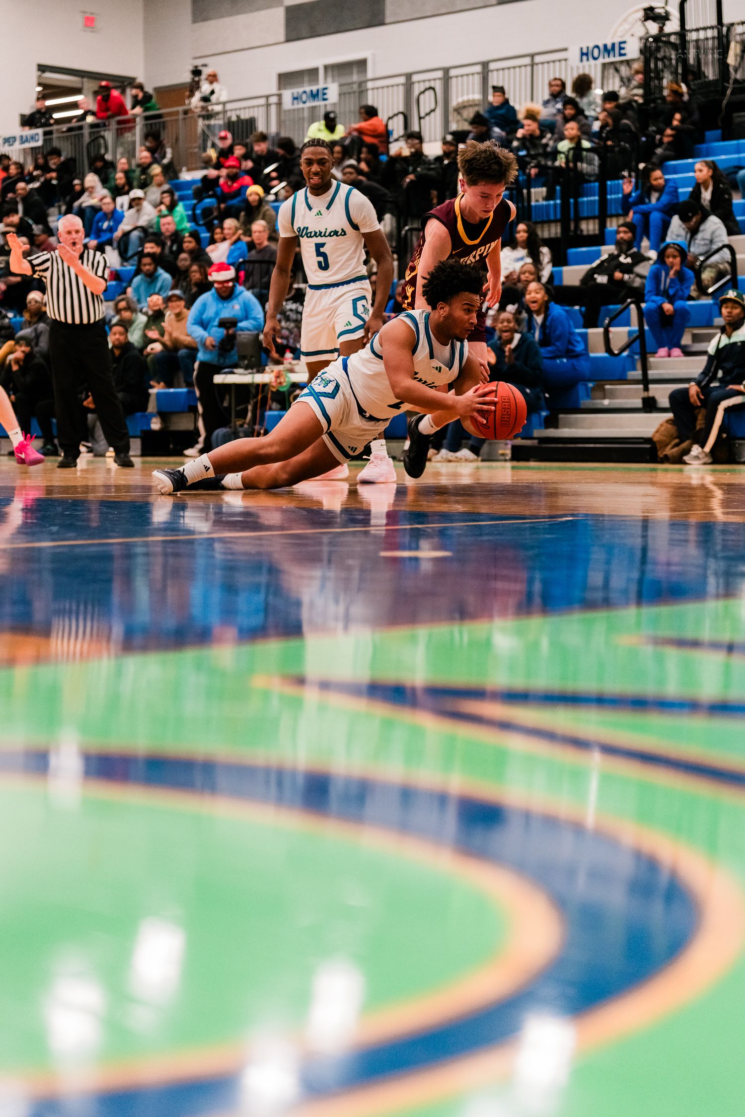 Warriors basketball player dives for a loose ball during an intense high school basketball game.