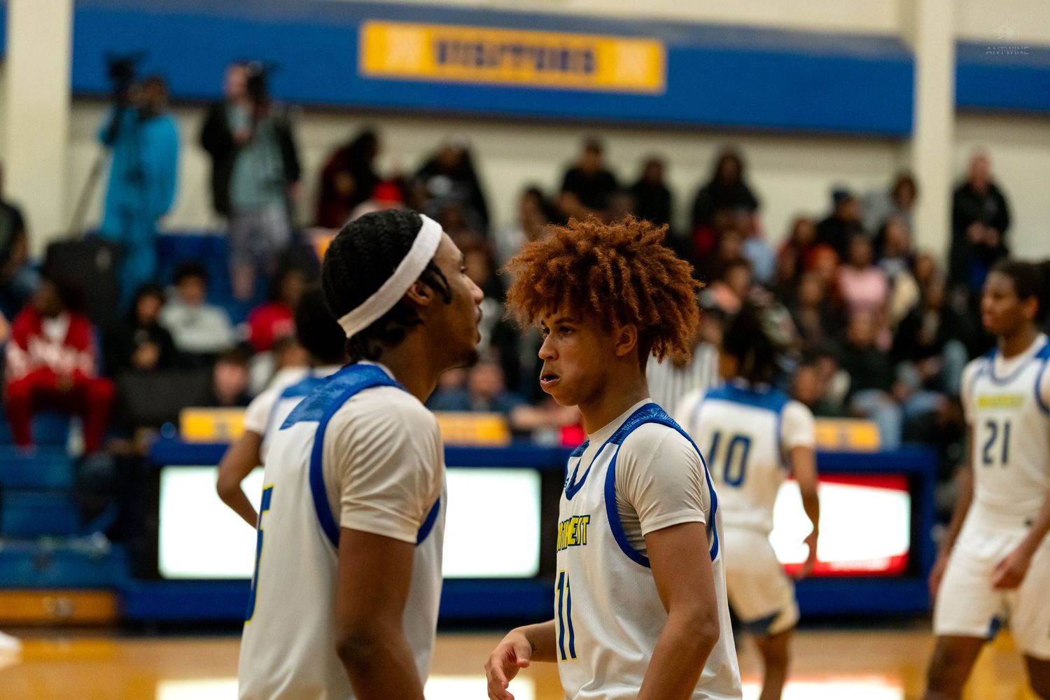 Two high school basketball teammates in white uniforms huddle together during a game timeout.