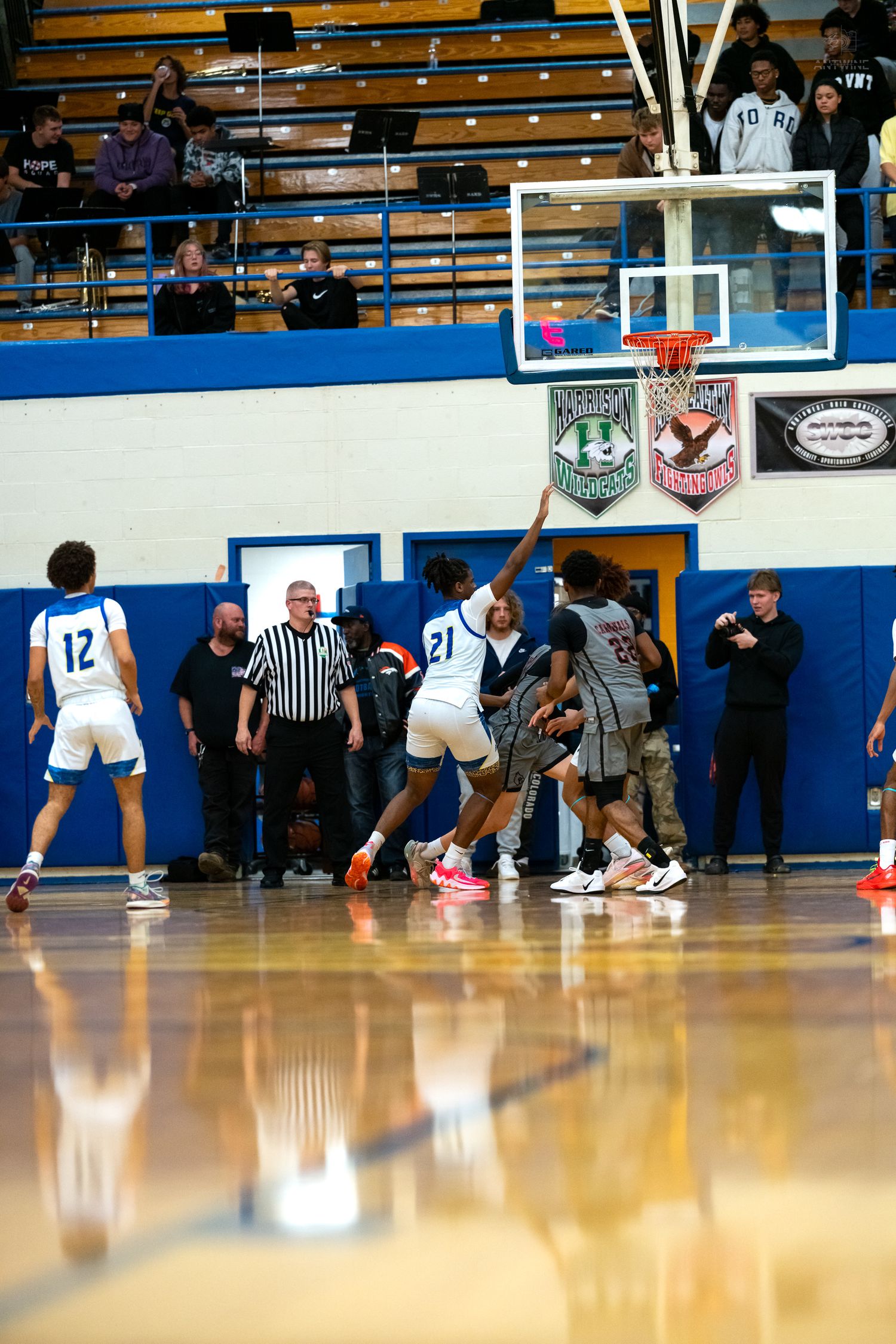 High school basketball players battle for rebound near basket during competitive indoor gymnasium game.