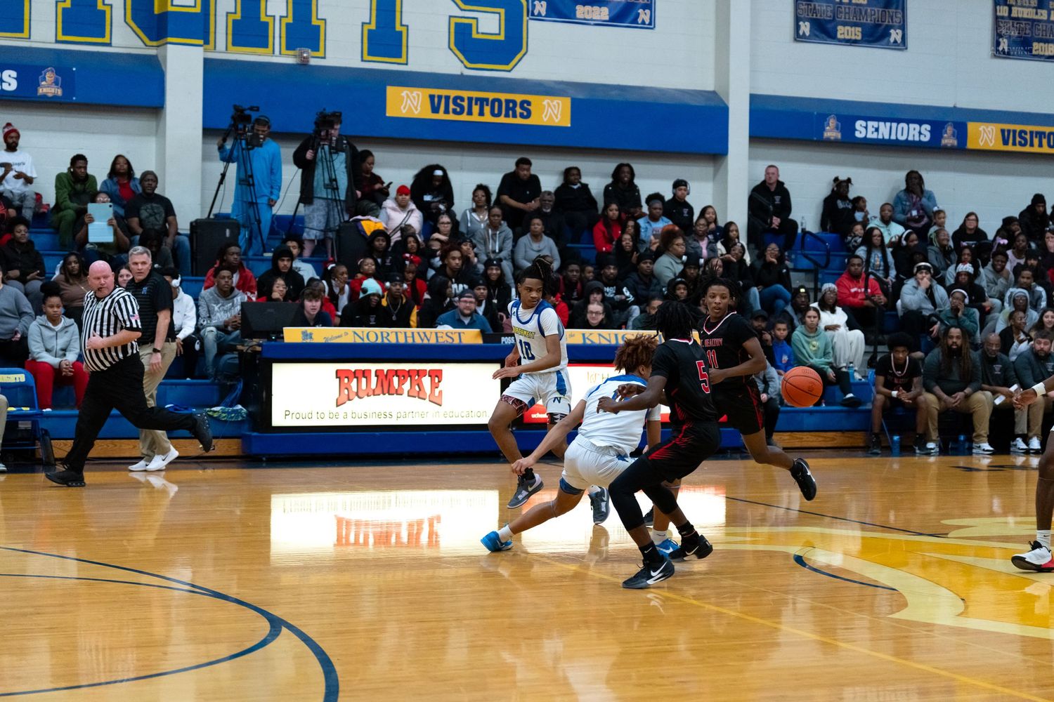 High school basketball game action shot with packed crowd watching players compete on indoor court.