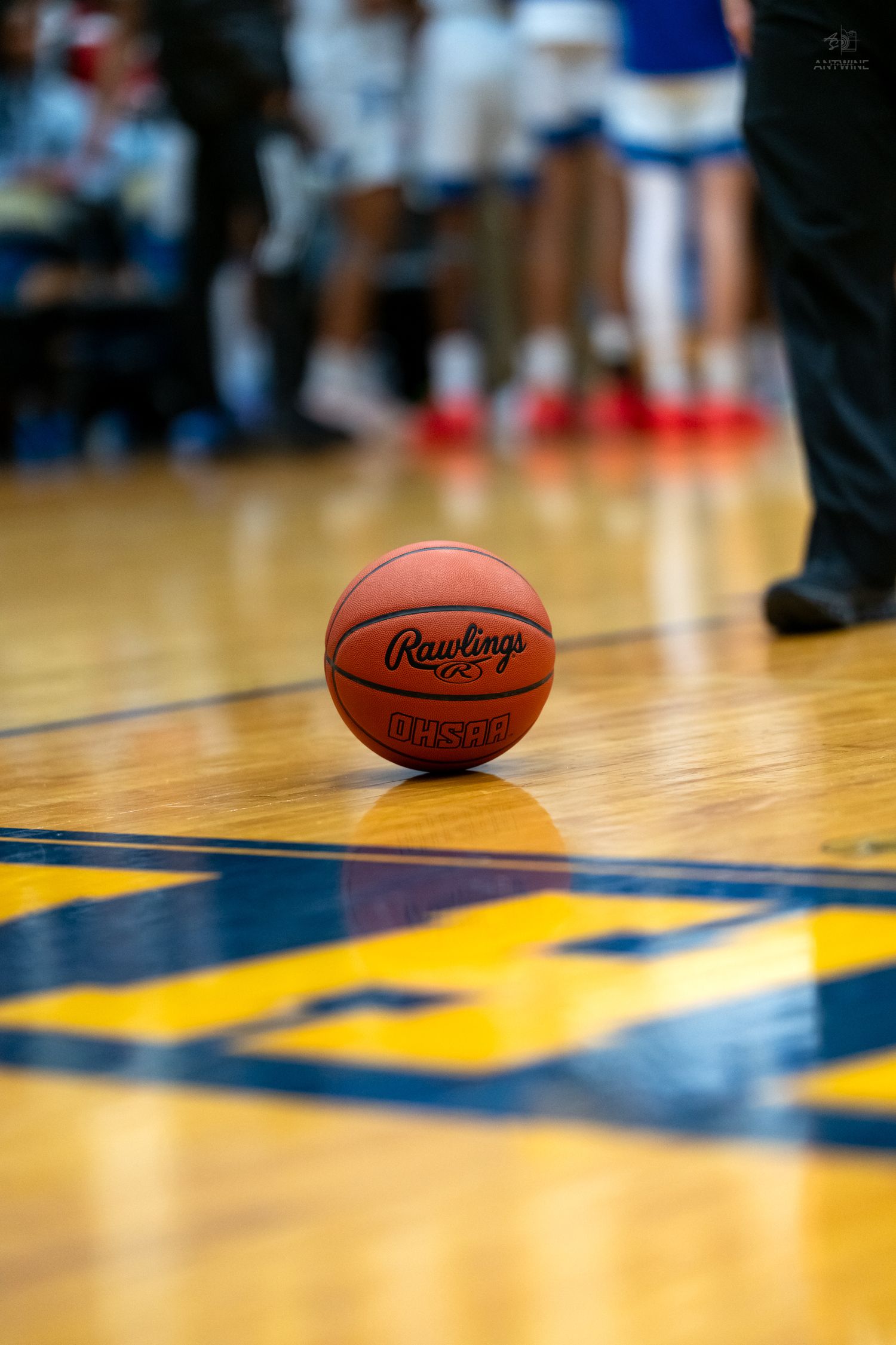 Rawlings NFHS basketball on a yellow and blue hardwood gymnasium floor during a basketball game.