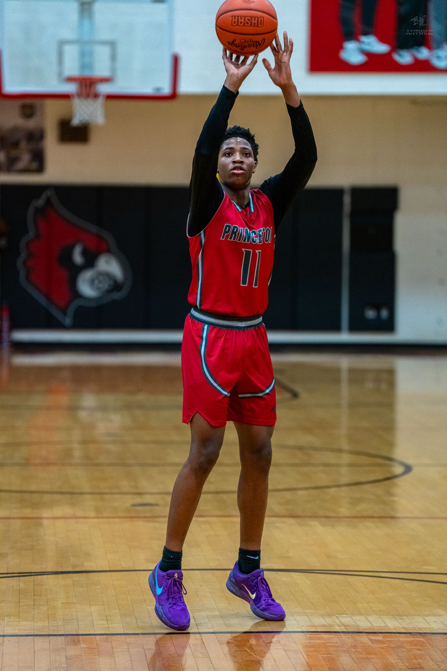 Basketball player #11 in red uniform shoots free throw in indoor gym.