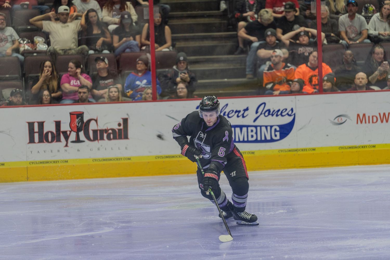 Hockey player in black uniform controlling the puck near the boards during a professional hockey game.