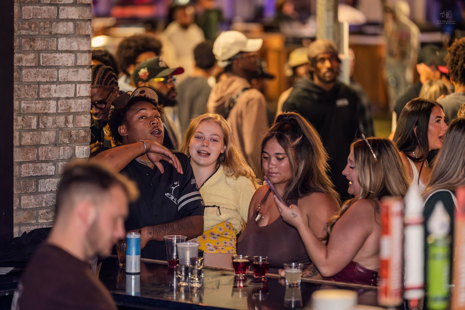 Group of smiling young women enjoying drinks and conversation at a lively nightclub bar.