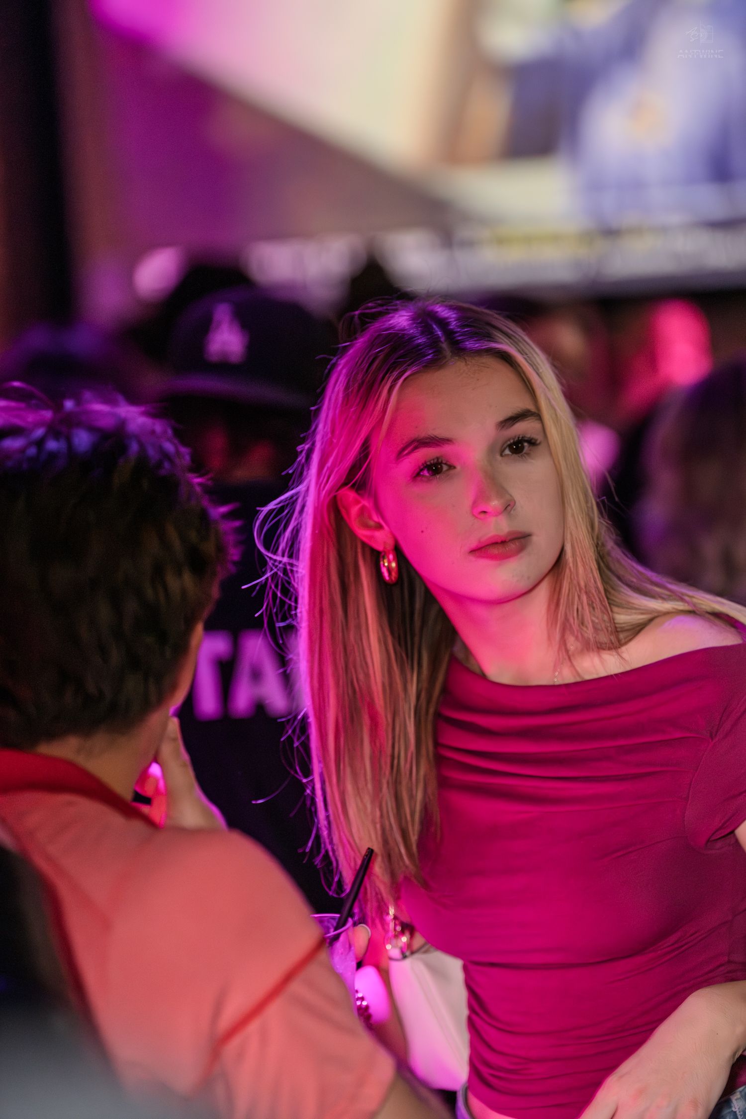 Young blonde woman in red off-shoulder top at a nightclub with purple lighting.