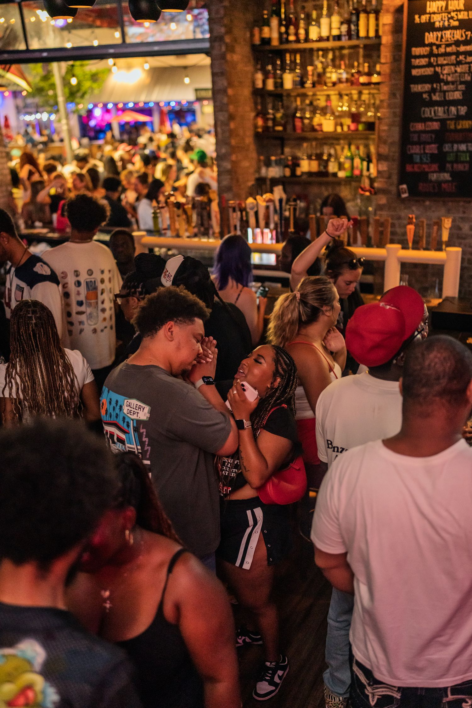 Crowded bar scene with diverse group of people socializing and dancing under warm lights at a busy nightclub.