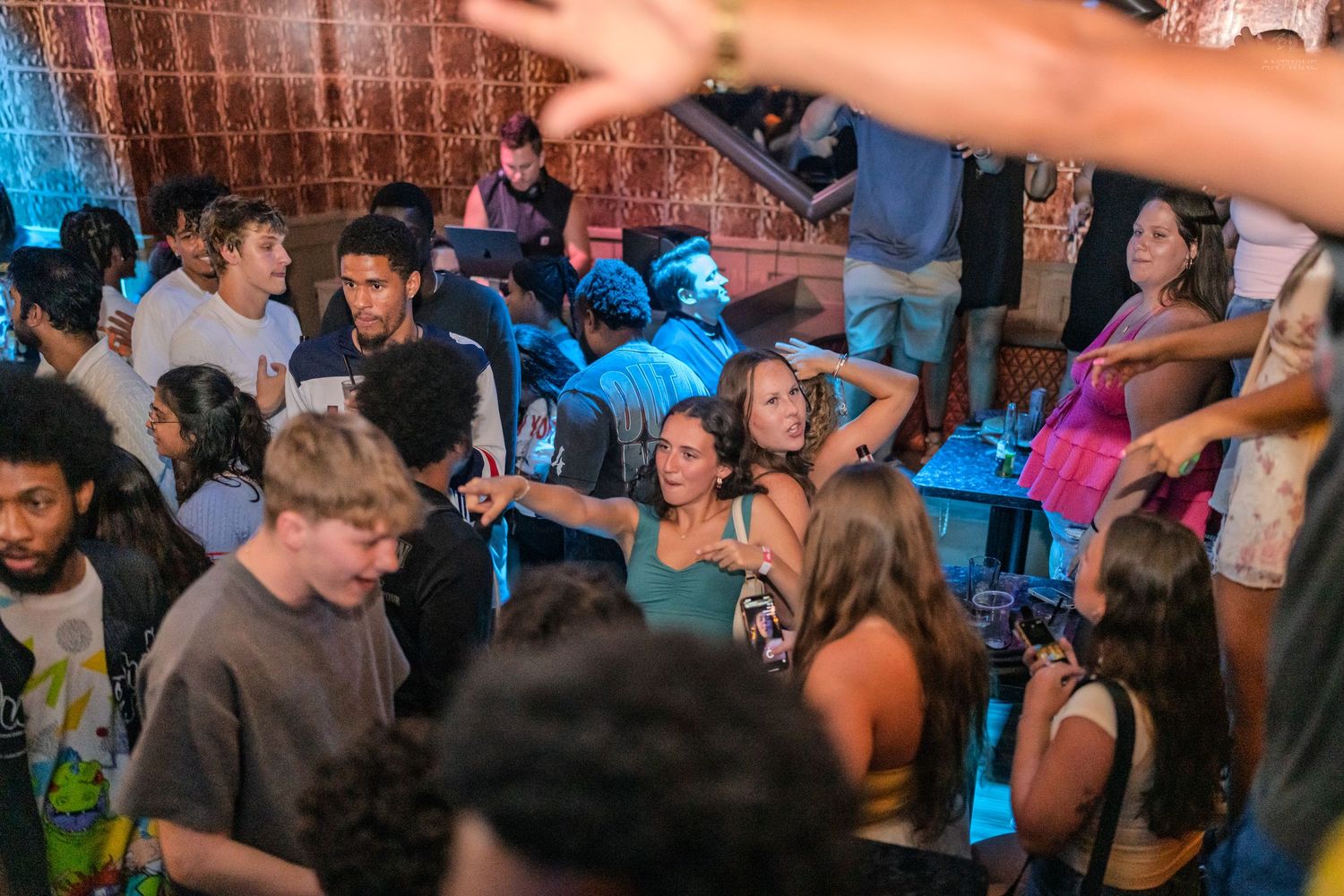 A lively group of young people socializing and dancing inside a crowded nightclub with blue lighting.