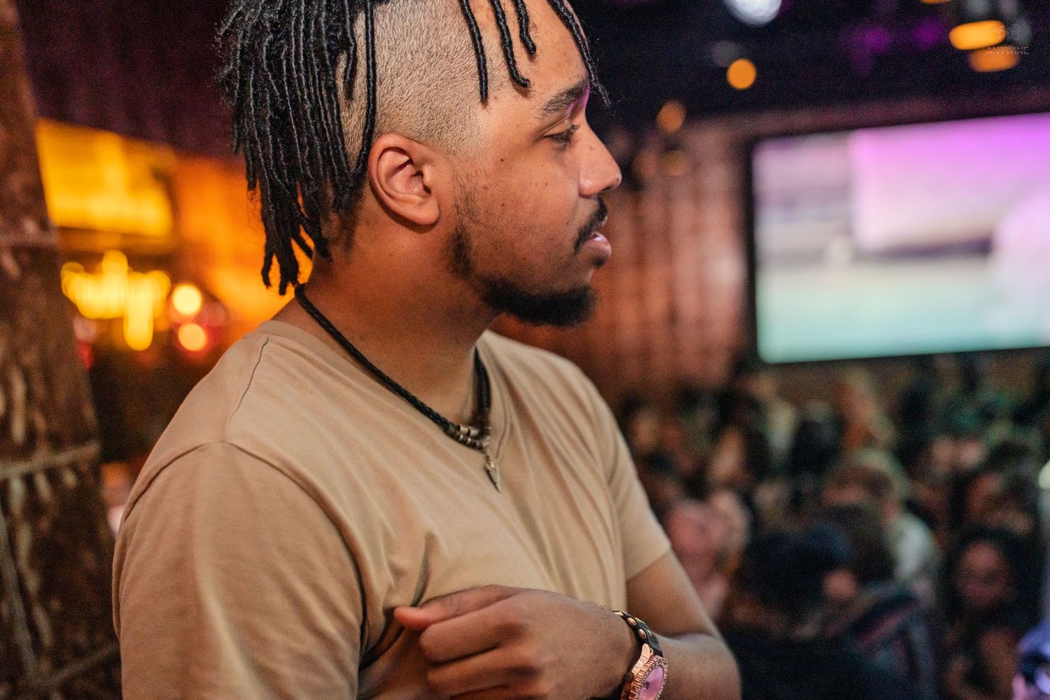 Close-up side profile of a bearded man with an afro at a colorful nightlife venue.